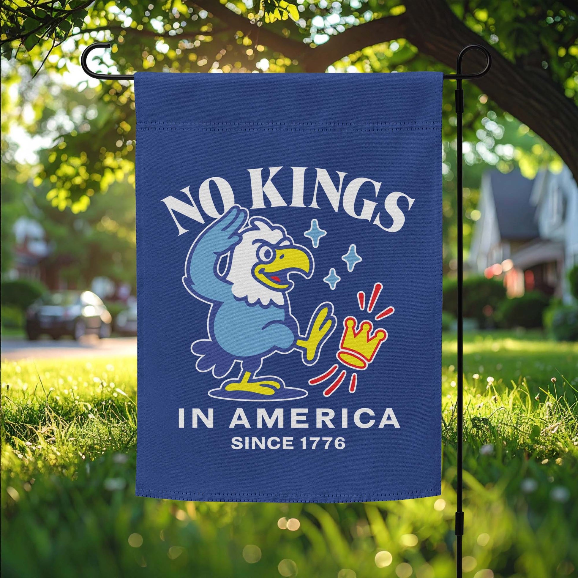 Garden flag featuring cartoon eagle graphic and the phrase “NO KINGS IN AMERICA SINCE 1776,” displayed on outdoor yard stake.