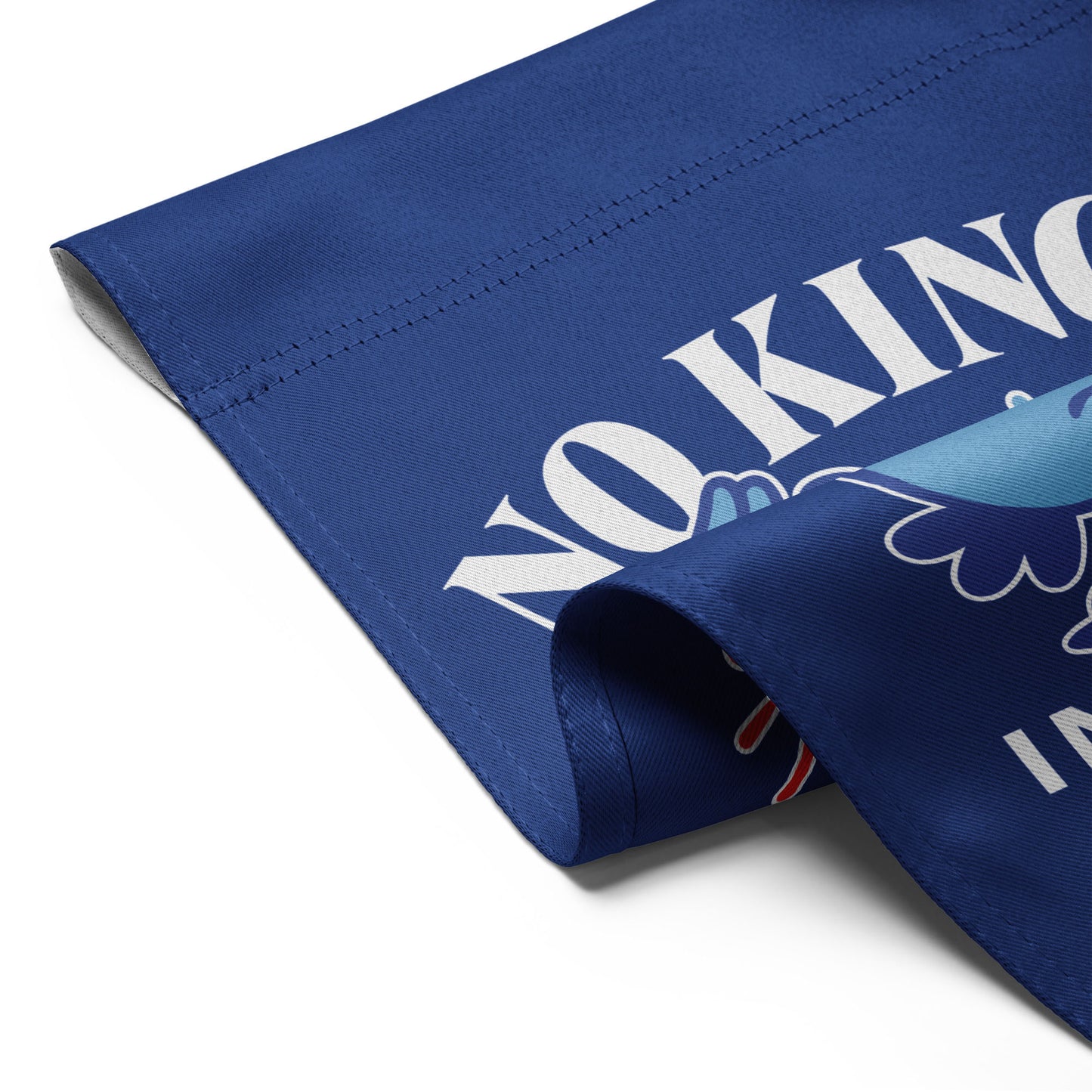Close-up of blue garden flag fabric showing partial eagle graphic and curved “NO KINGS” lettering from the phrase “NO KINGS IN AMERICA SINCE 1776.”