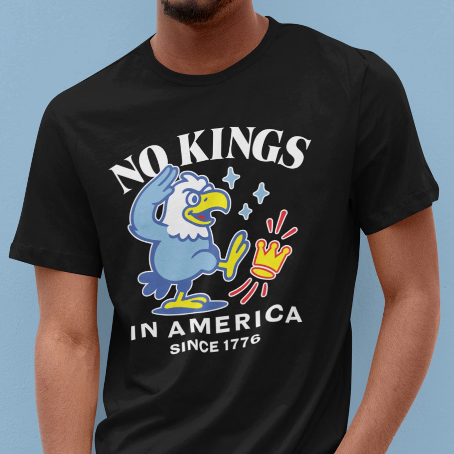 Model wearing black unisex t-shirt displaying cartoon eagle illustration and the slogan “NO KINGS IN AMERICA SINCE 1776.”