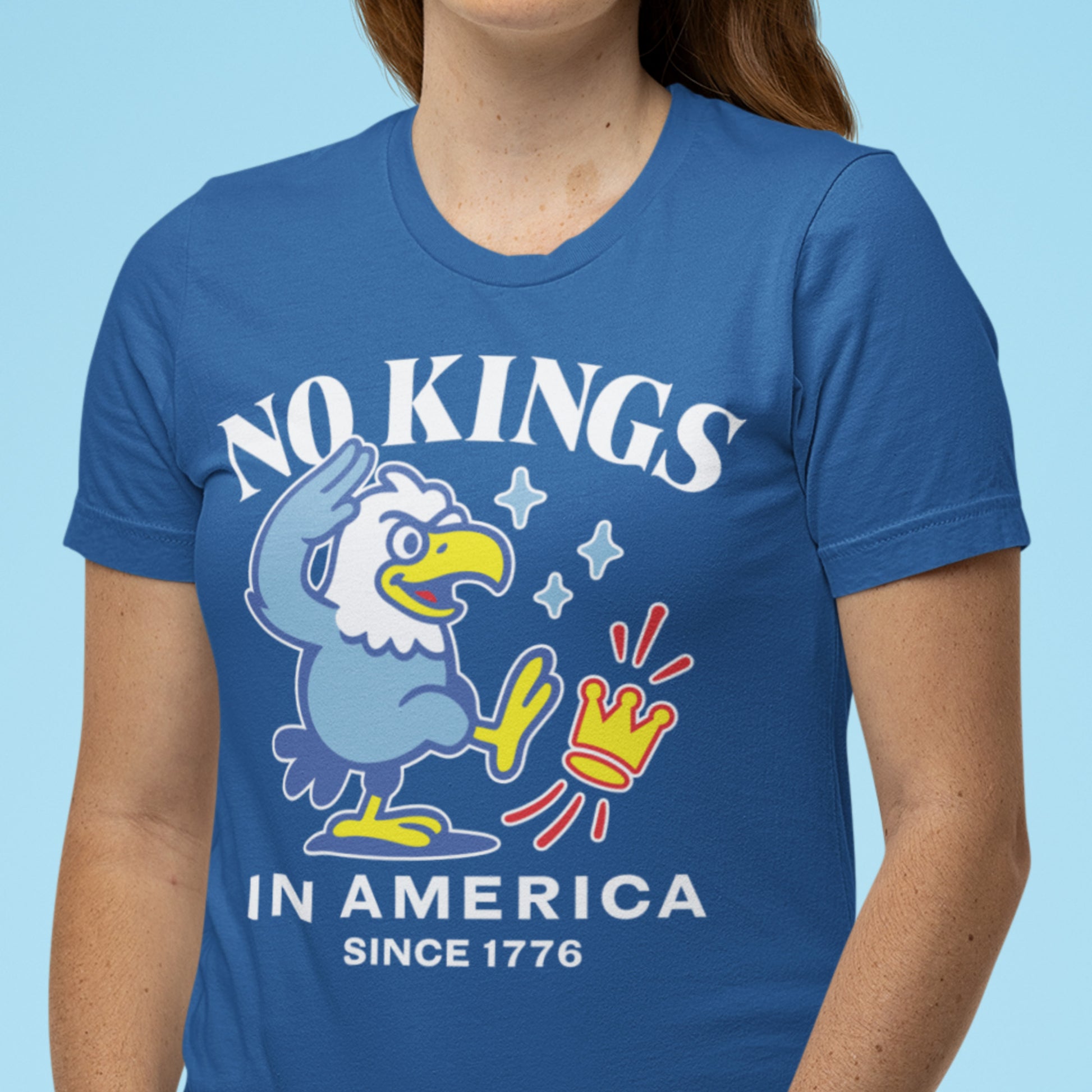 Model wearing royal blue unisex t-shirt featuring patriotic eagle artwork with text reading “NO KINGS IN AMERICA SINCE 1776.”