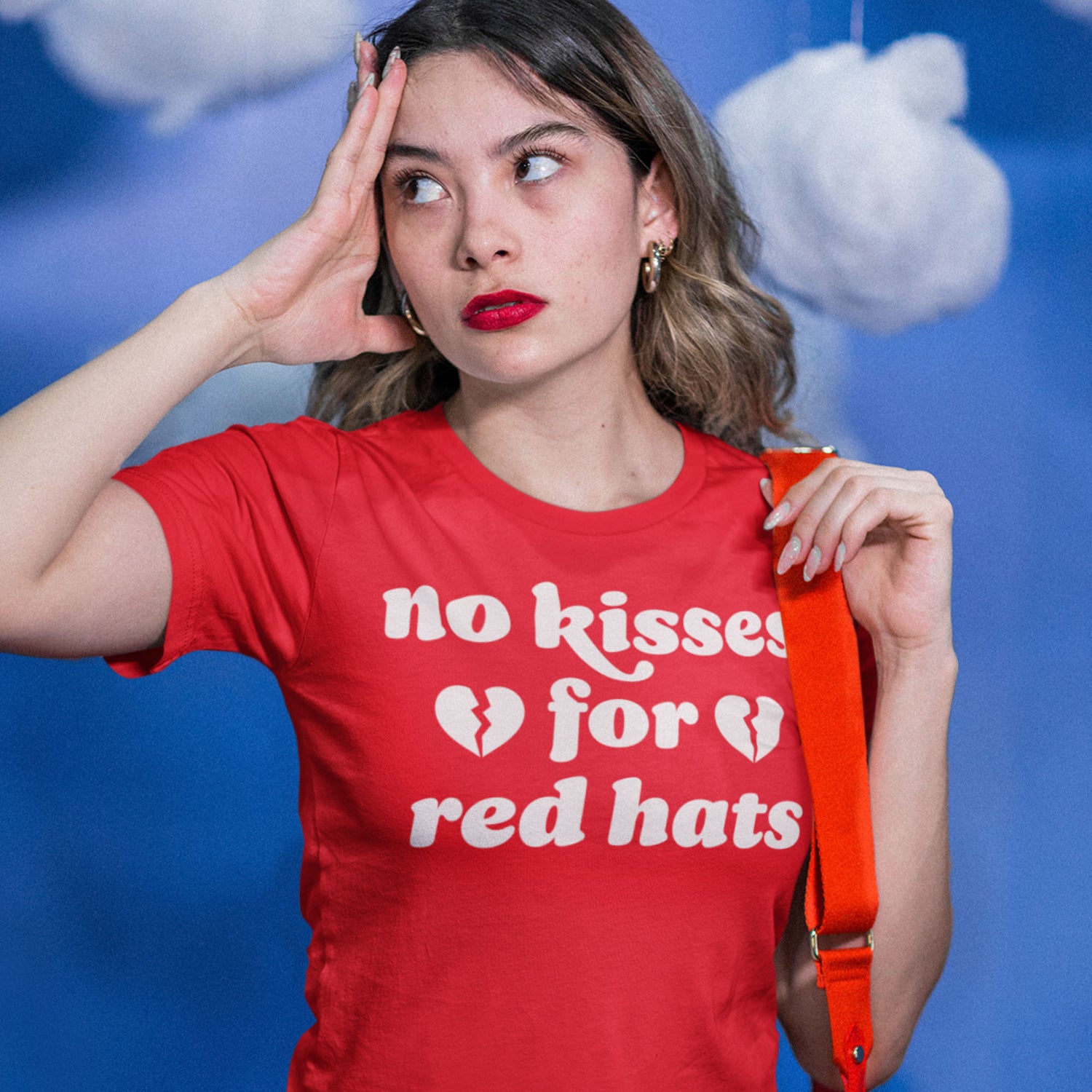 Woman wearing a red unisex t-shirt with bold retro lettering and broken heart icons reading “no kisses for red hats,” a progressive anti-MAGA apparel design styled for everyday activism.