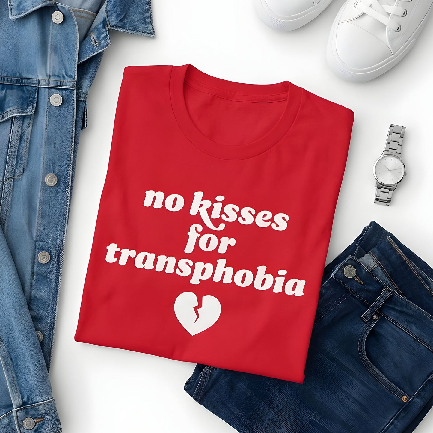 Flat lay of red unisex t-shirt styled with denim and accessories, showcasing retro lettering and broken heart artwork with the phrase “no kisses for transphobia,” progressive apparel.