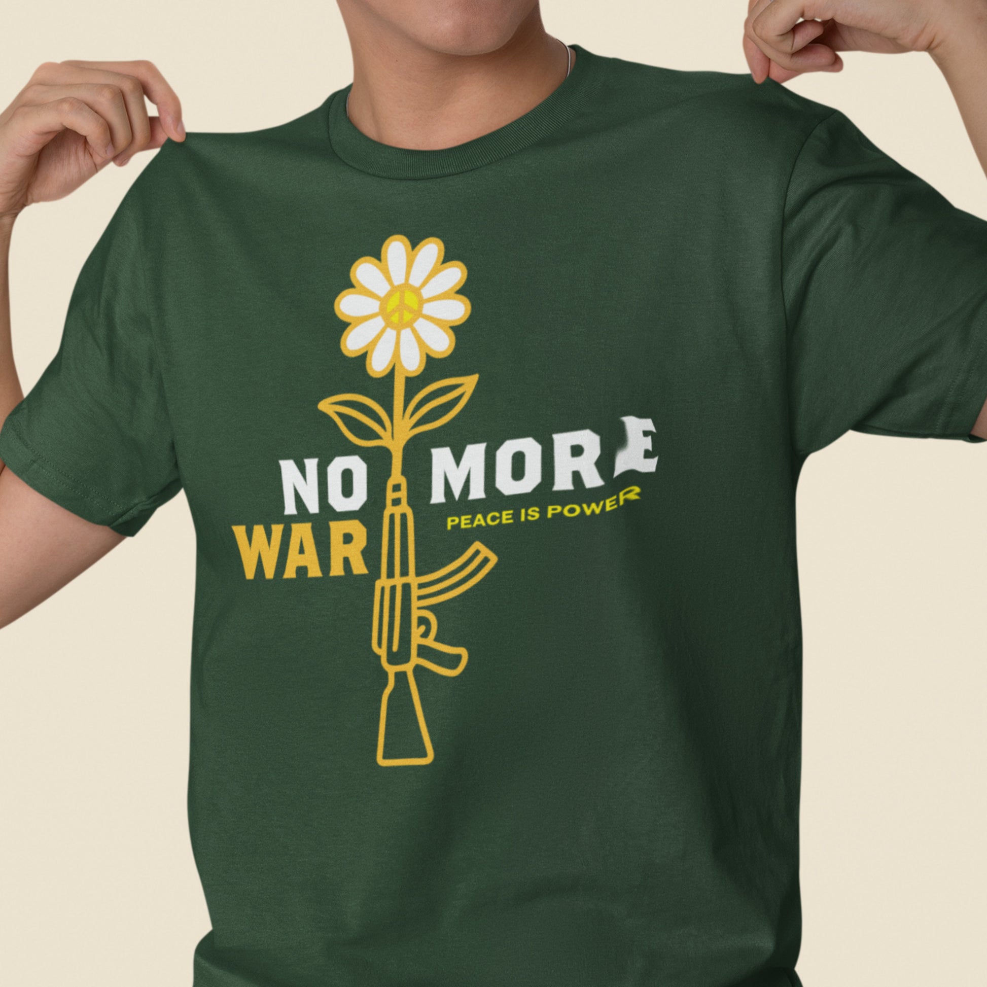 Model wearing green unisex t-shirt displaying daisy-and-rifle graphic with “NO MORE WAR” slogan and subtle peace statement beneath.