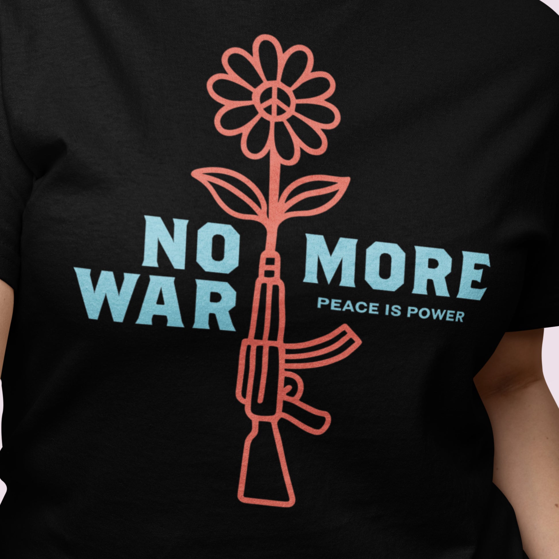 Close-up of black women’s relaxed tee showing line-art rifle blooming into flower with “NO MORE WAR” message and subtle “PEACE IS POWER” wording.