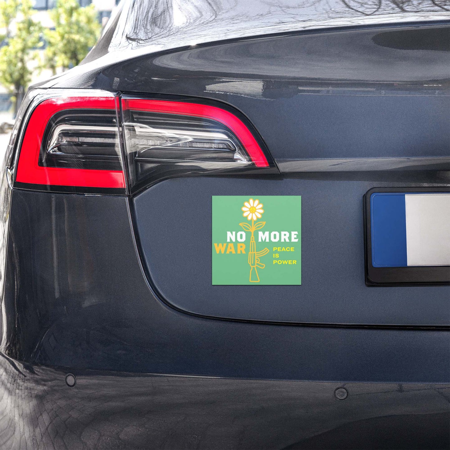 Green car magnet with floral rifle artwork and “NO MORE WAR” peace statement displayed on rear of vehicle bumper.