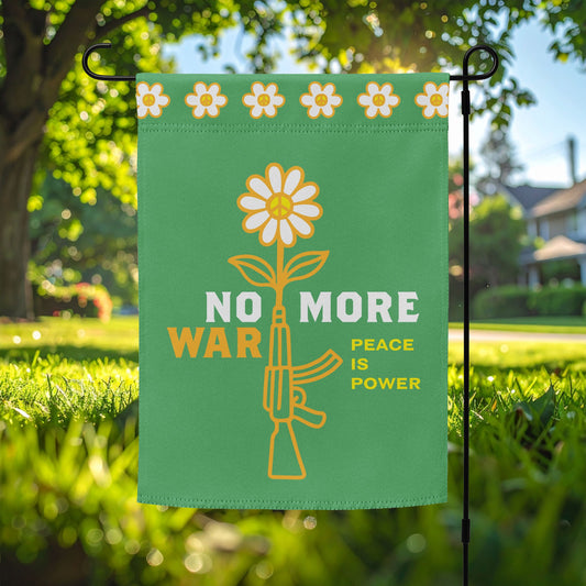 Garden flag featuring yellow daisy growing from rifle graphic with bold “NO MORE WAR” and smaller “PEACE IS POWER” message displayed on lawn stake outdoors.