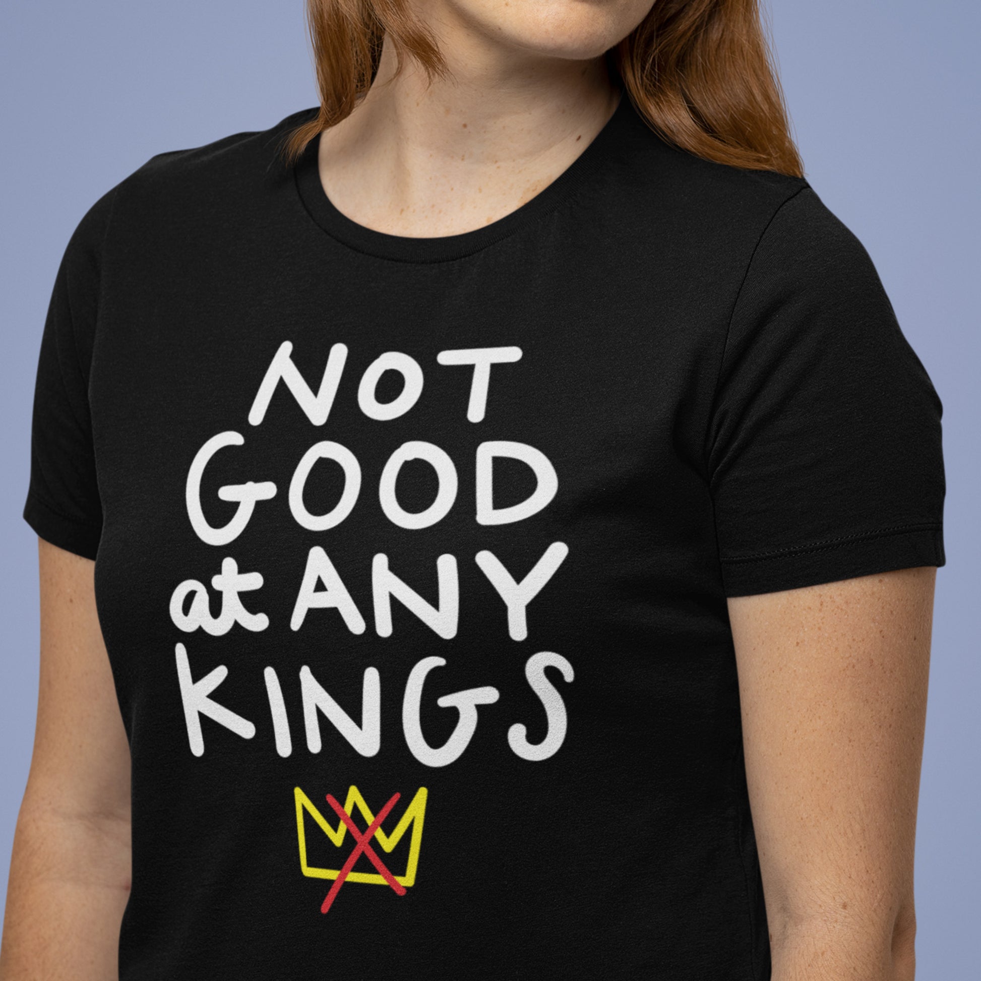 Model wearing black unisex t-shirt with bold white lettering reading “NOT GOOD AT ANY KINGS” and small crown graphic.