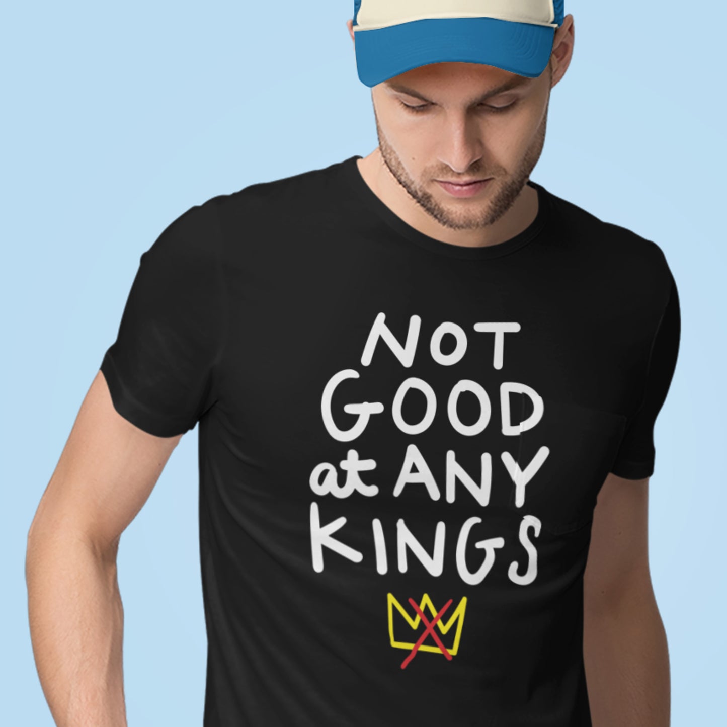 Model wearing black unisex t-shirt displaying the phrase “NOT GOOD AT ANY KINGS” with colorful crown icon.