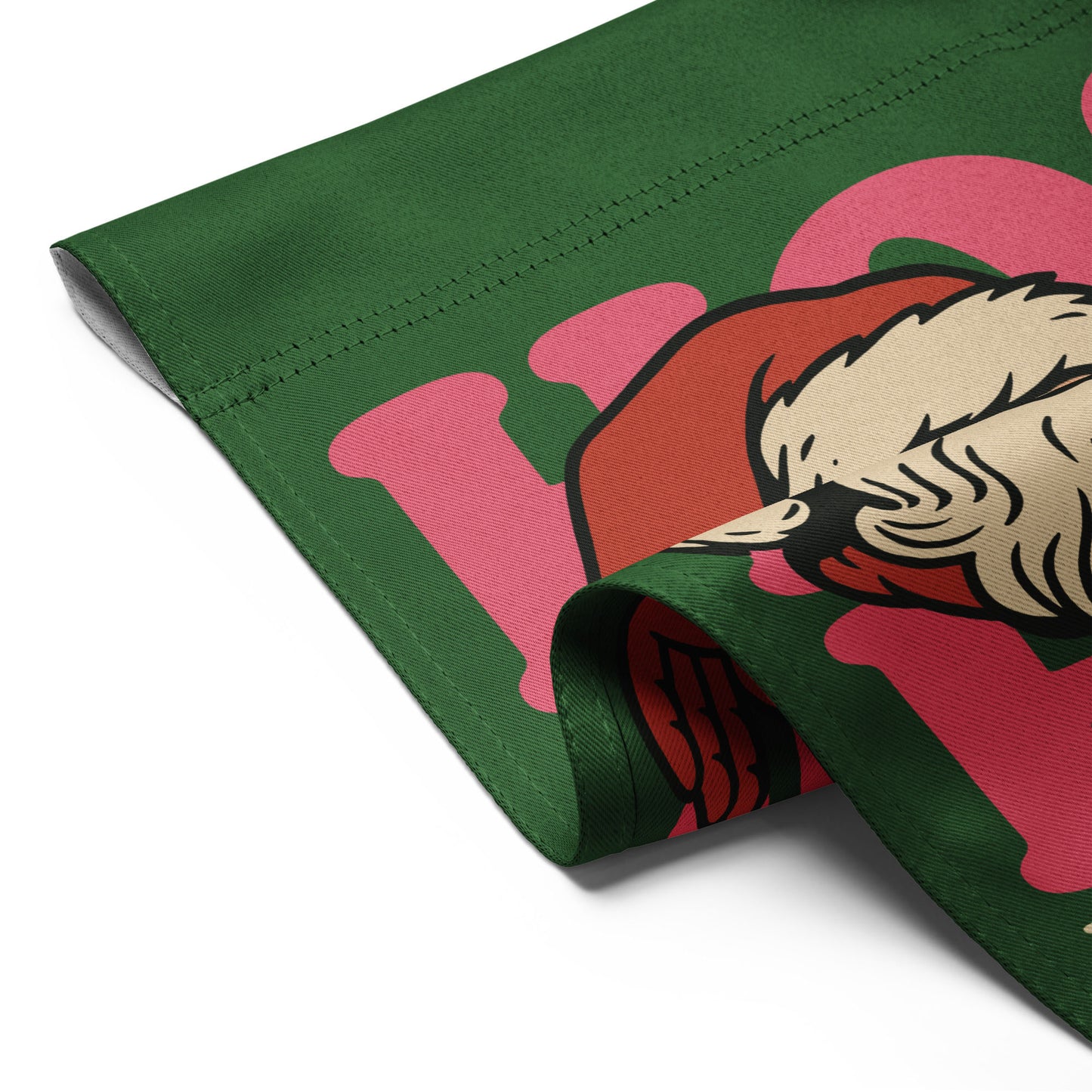 Close-up of a folded green garden flag showing part of a retro Santa illustration, pink “HO!” lettering, and the printed message “Peace and Justice for All.”