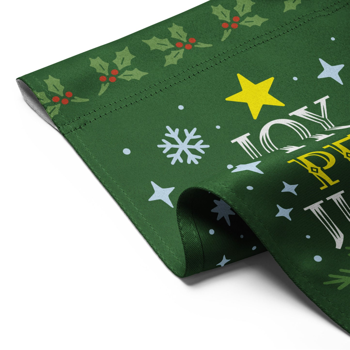 Angled close-up of a green garden flag showing decorative stars, snowflakes, and lettering that reads “JOY LOVE HOPE PEACE JUSTICE.”