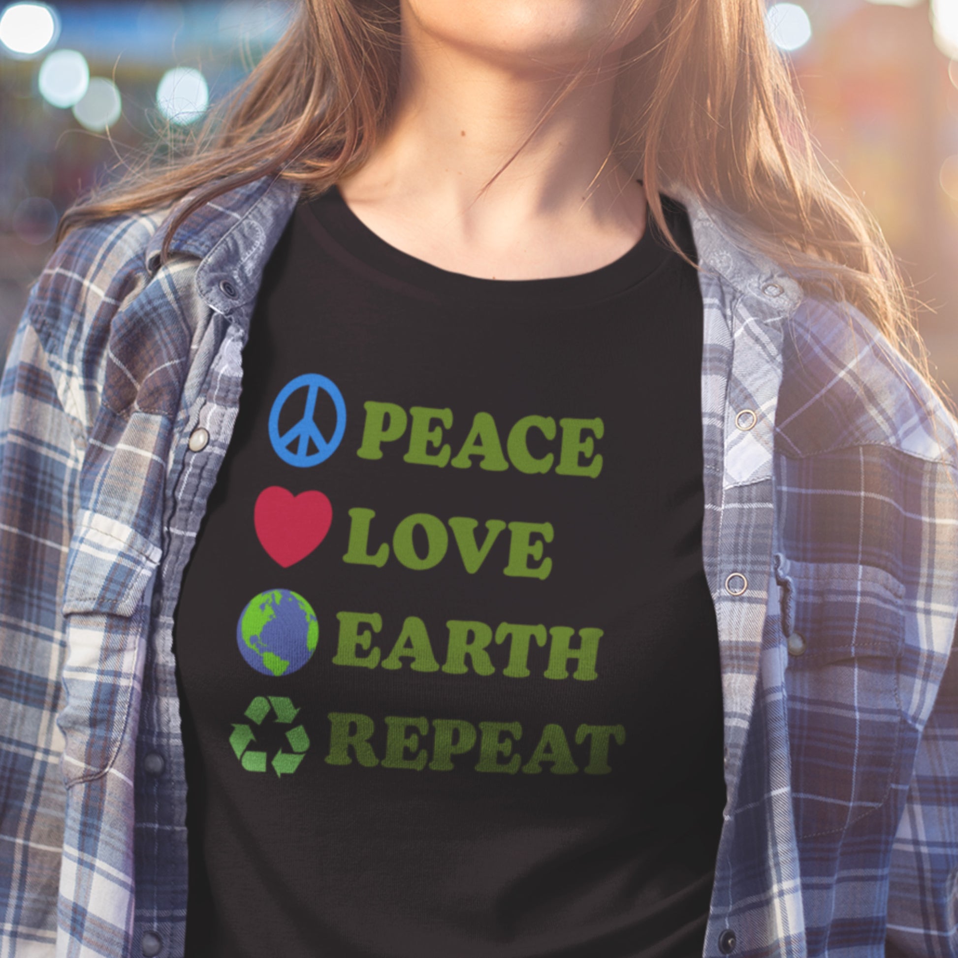 Model wearing “Peace Love Earth Repeat” black t-shirt with green activist message, styled with plaid shirt.