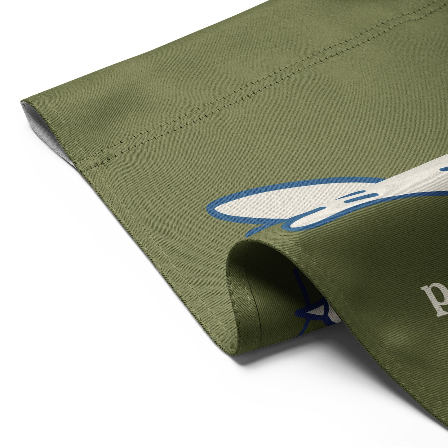 Close-up folded garden flag corner showing olive green fabric texture with partial white dove artwork and visible blue outline detail.