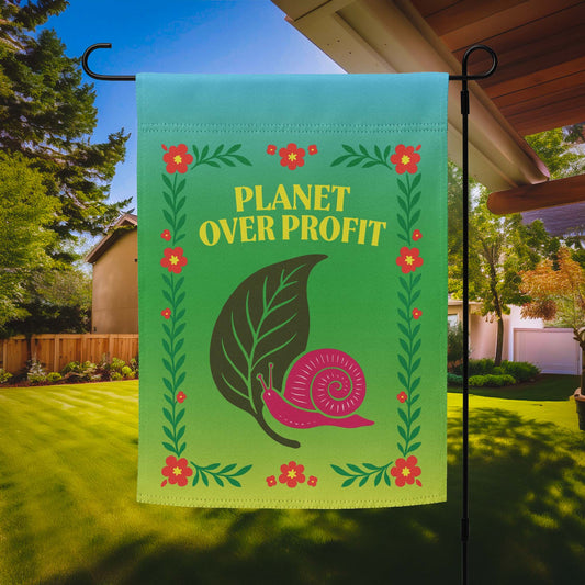 “Planet Over Profit” eco-activist garden flag with snail and leaf design surrounded by floral border, displayed outdoors on a flag stand.