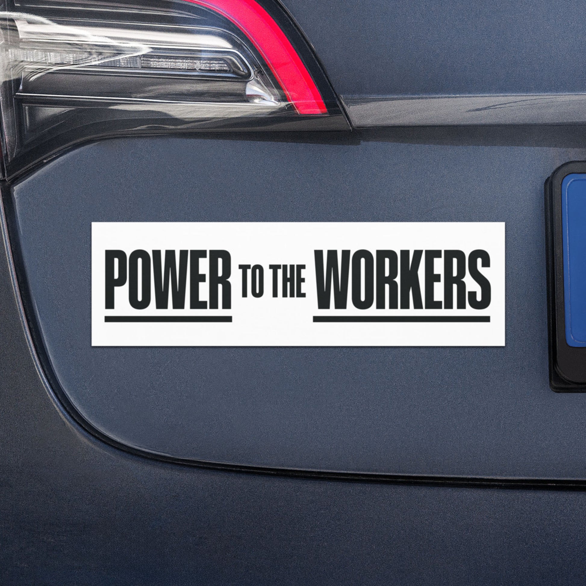 Car magnet applied to vehicle bumper displaying “Power to the Workers” slogan in strong minimalist typography, emphasizing labor rights and worker solidarity message.