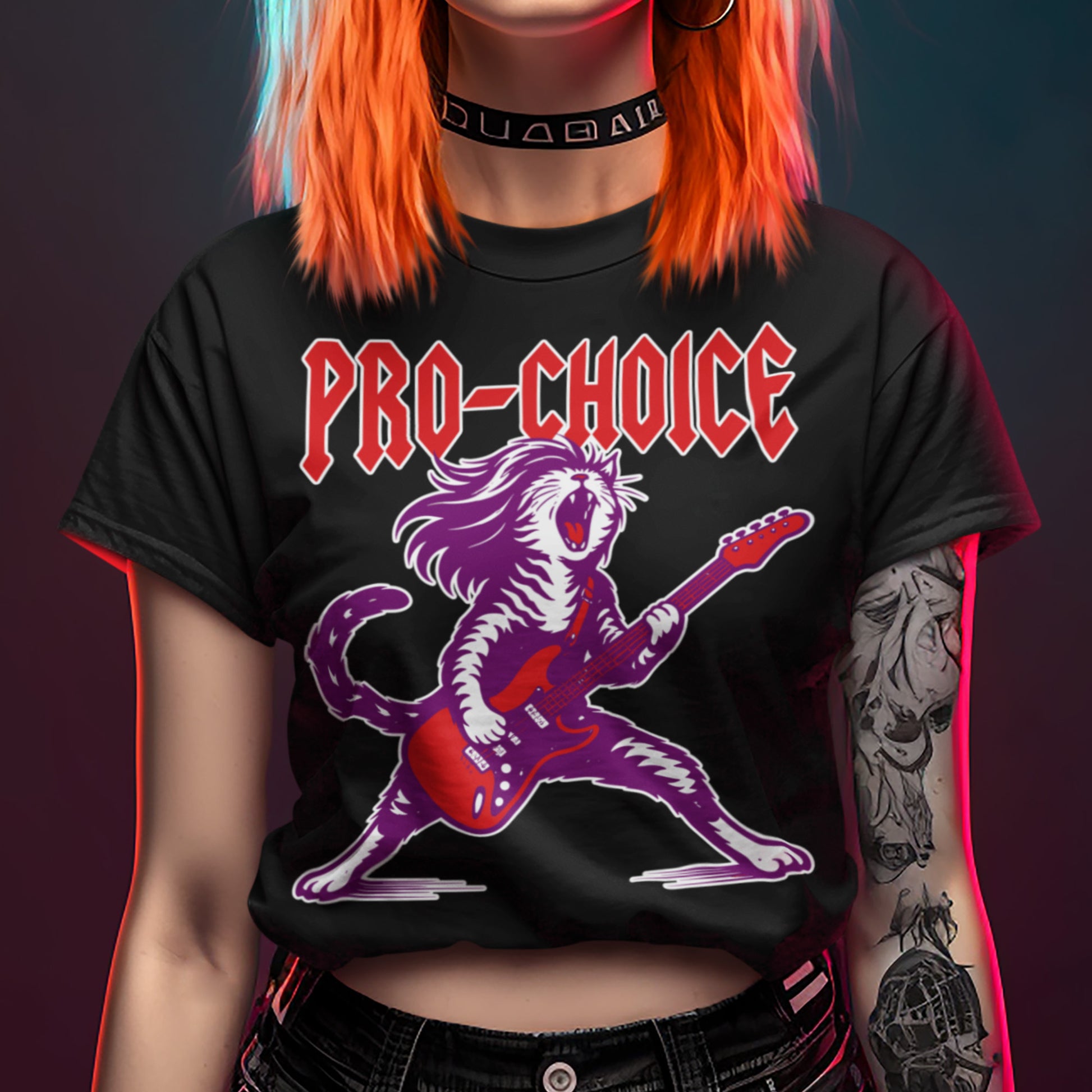 Model wearing a black women’s relaxed t-shirt with a rockstar cat illustration holding a guitar and the text “PRO-CHOICE,” cropped styling shown in a studio setting from Blue Wave USA.