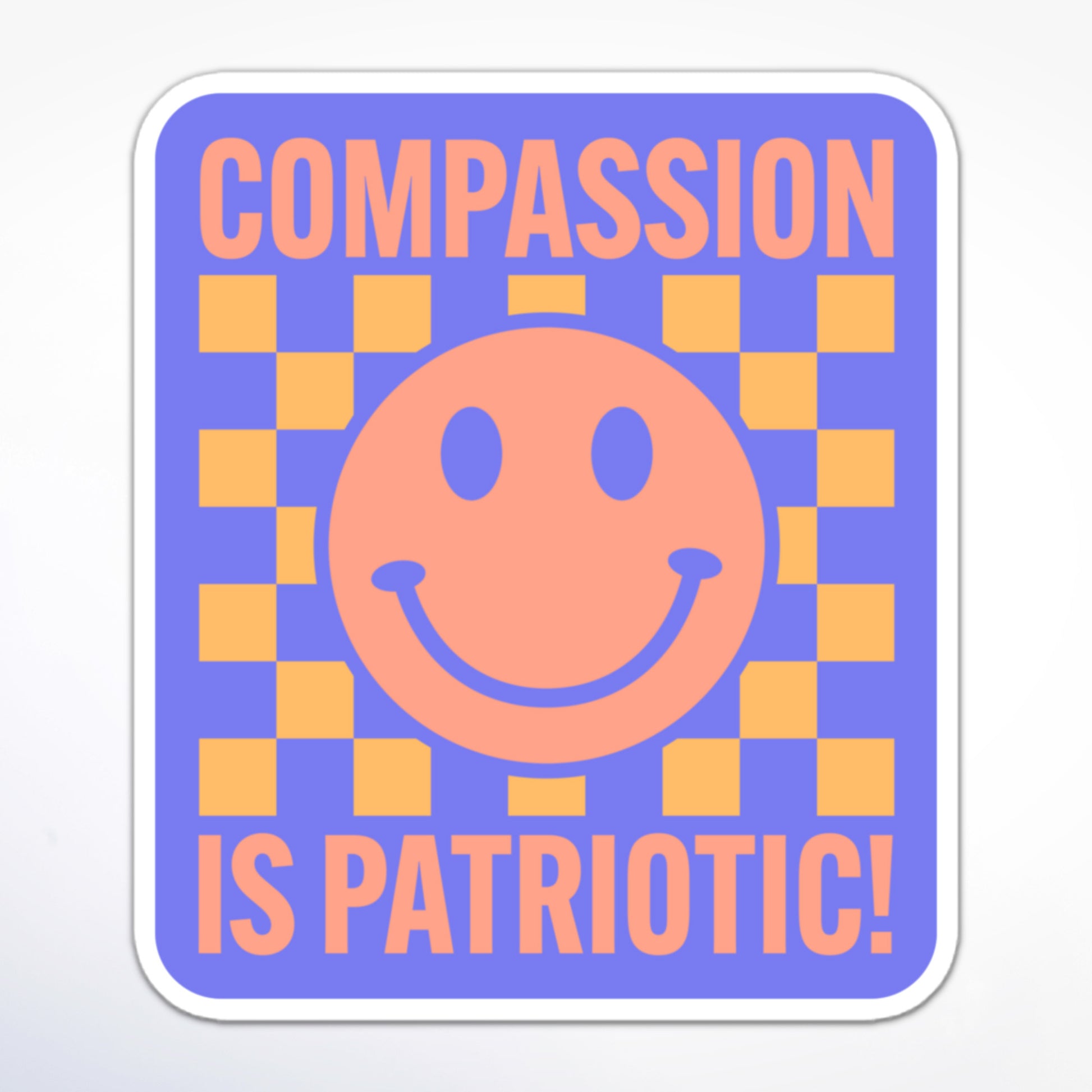 Progressive activism sticker with a happy face, yellow and purple checkerboard, and the message “Compassion is Patriotic!” in a bold font.