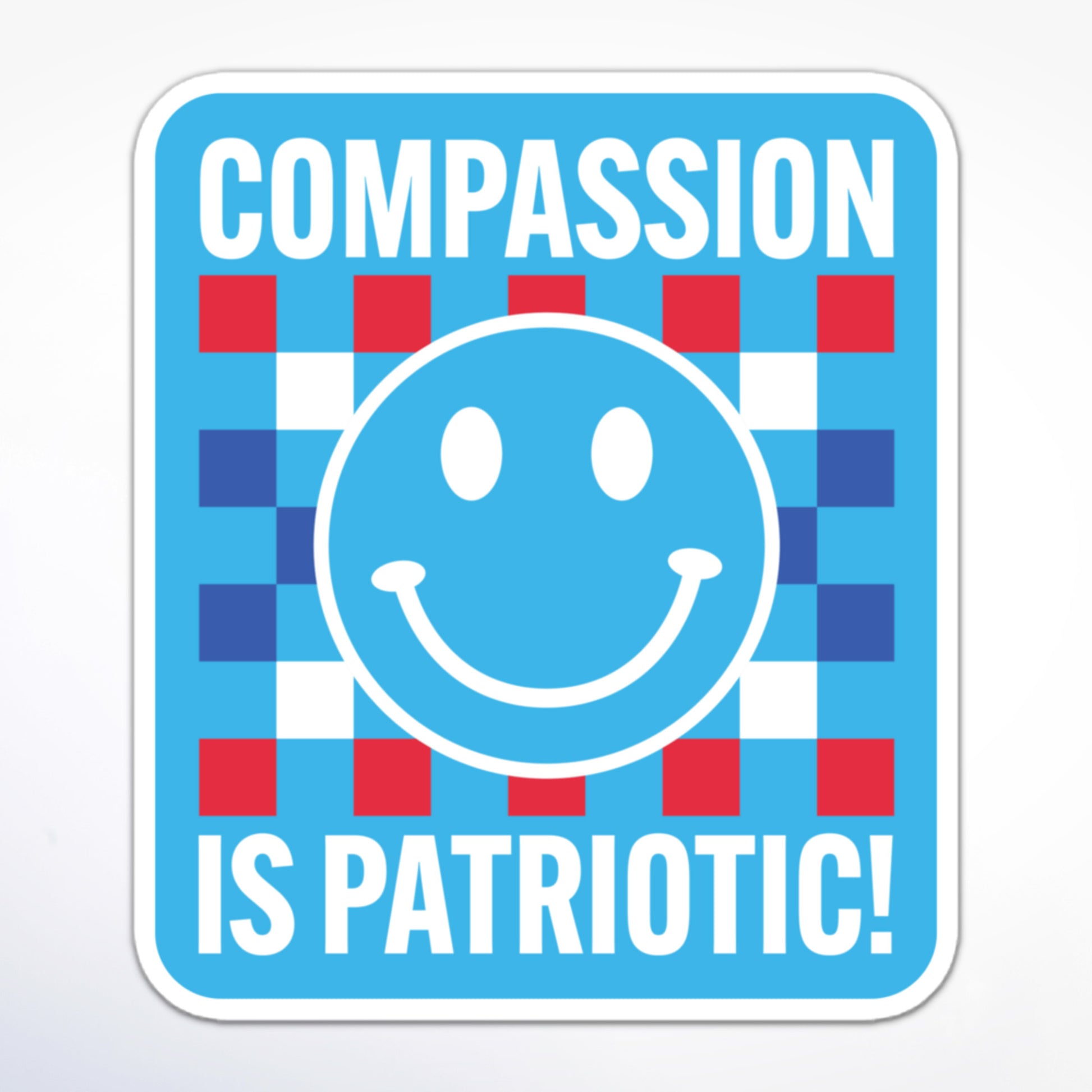 Social justice sticker with a blue smiley face, checkered pattern, and patriotic colors, displaying the message “Compassion is Patriotic!” in white block text.