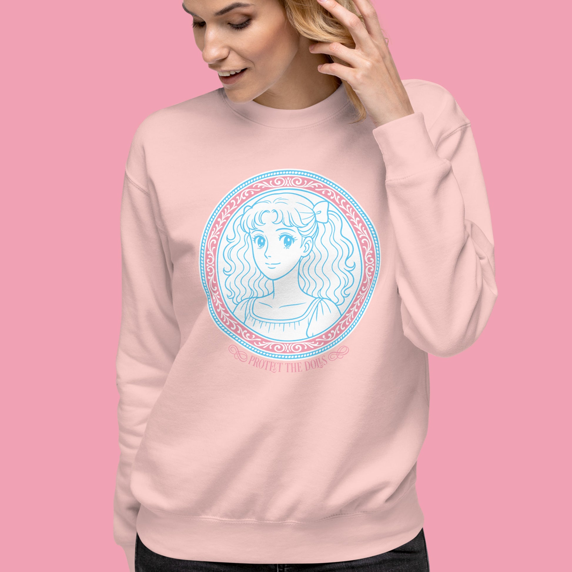 Light pink unisex premium sweatshirt worn by model against soft pink background, showcasing pastel blue illustrated portrait artwork and the phrase “Protect The Dolls Trans Rights.”