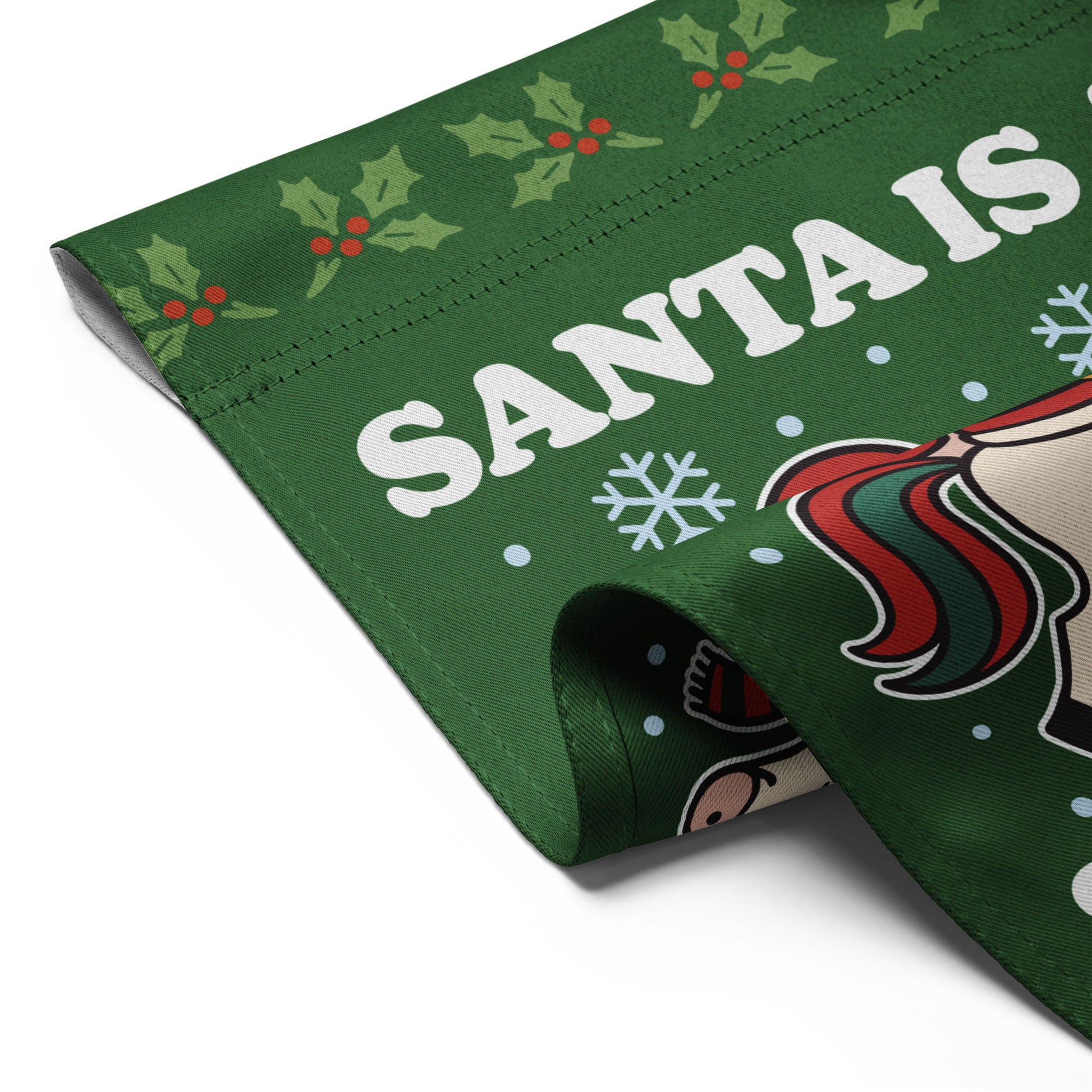 Close-up of a folded green garden flag showing part of a retro Santa riding a unicorn illustration, snowflakes, and the printed message “SANTA IS A SOCIALIST.”