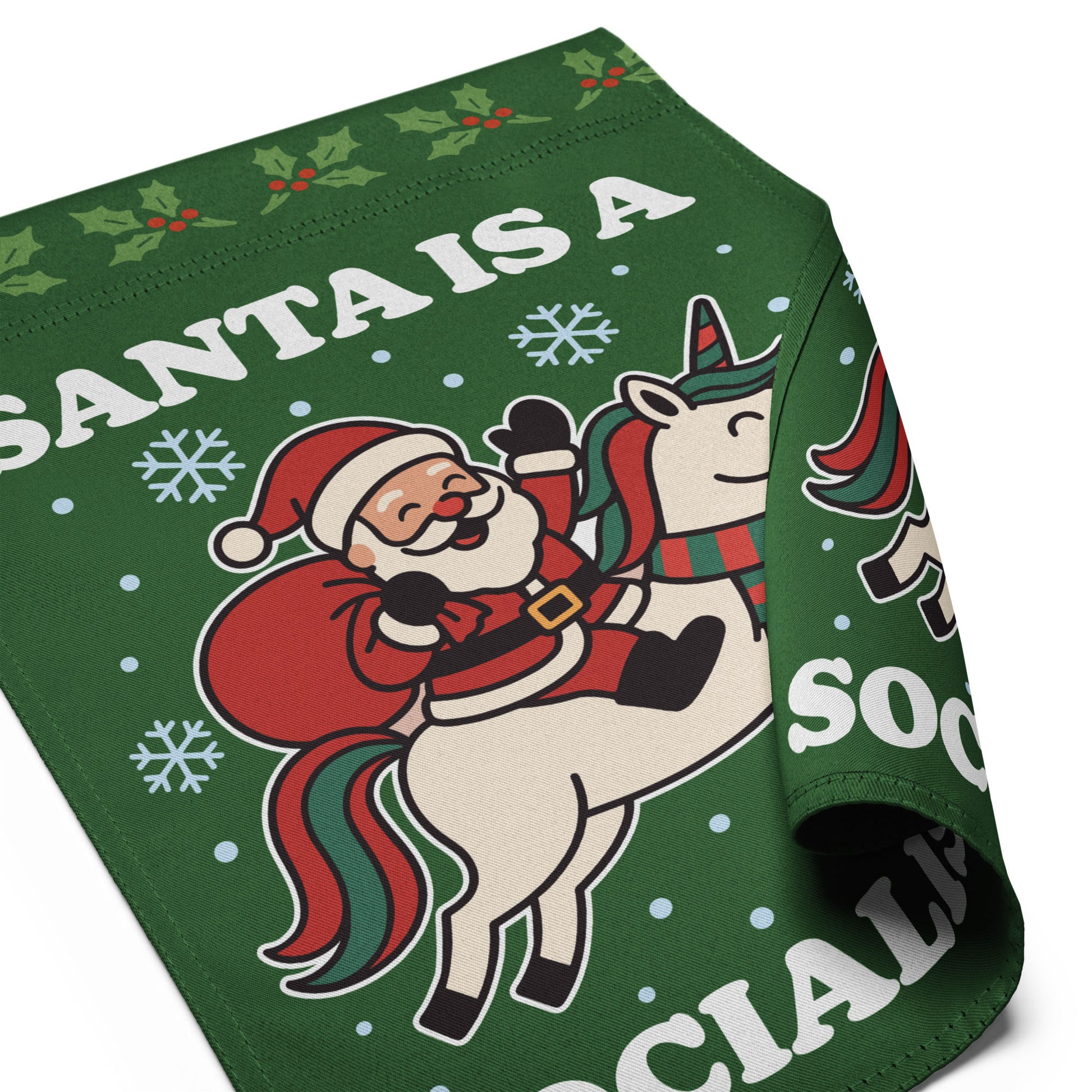 Close-up of rolled green garden flag fabric displaying partial retro Santa riding a unicorn artwork, snowflakes, and the printed phrase “SANTA IS A SOCIALIST.”