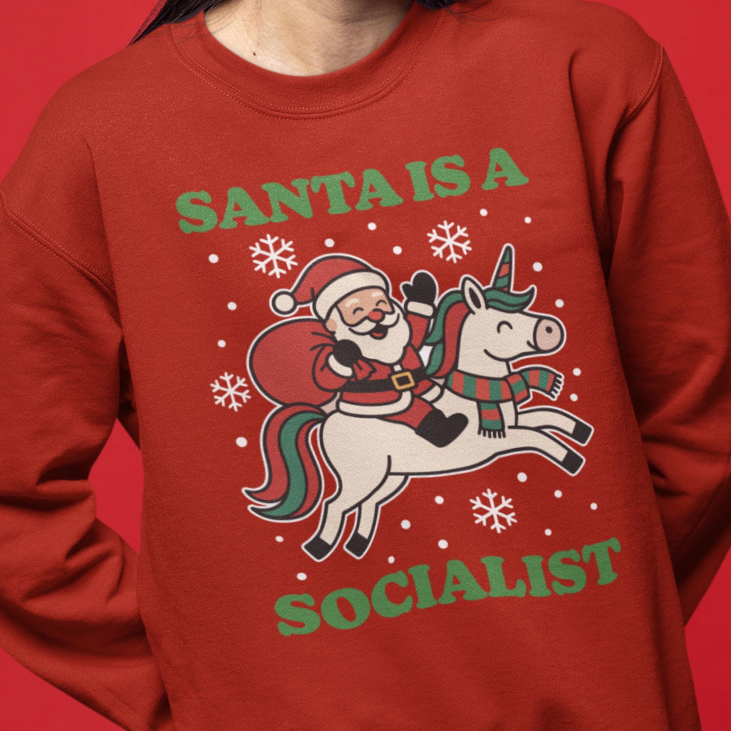 Model wearing a red sweatshirt featuring a vintage-style Santa riding a unicorn with stars and the printed phrase “SANTA IS A SOCIALIST.”