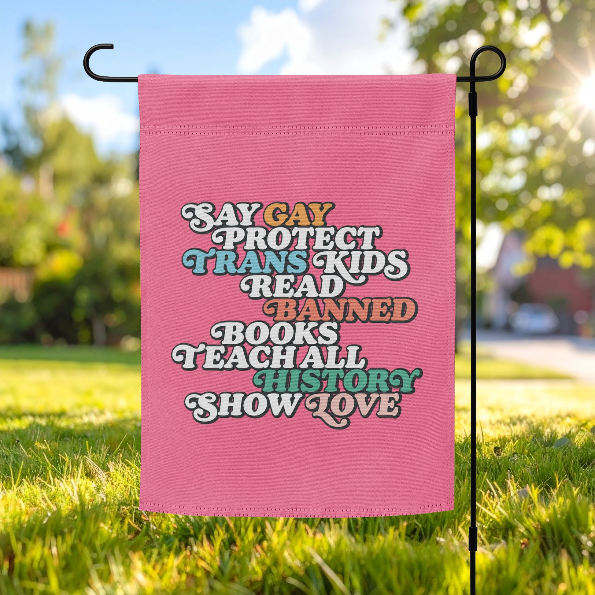 Pink garden flag displayed on outdoor pole featuring retro stacked typography reading “Say Gay Protect Trans Kids Read Banned Books Teach All History Show Love,” progressive decor from Blue Wave USA.