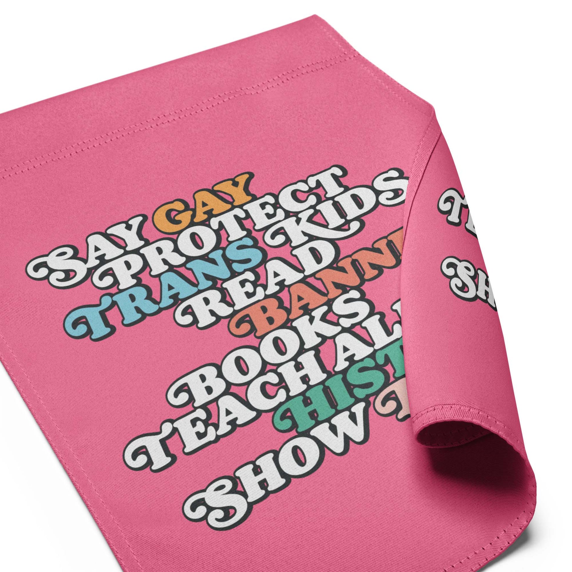 Pink garden flag fabric close-up showing retro stacked typography reading “Say Gay Protect Trans Kids Read Banned Books Teach All History Show Love.”