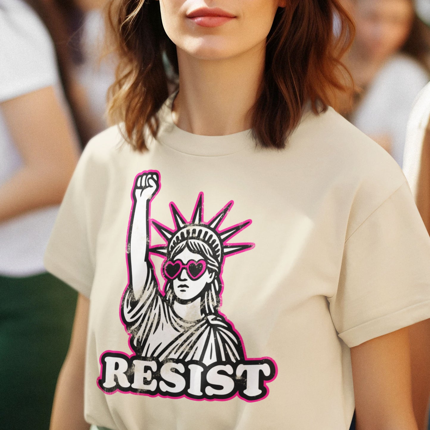 Model wearing a cream “RESIST” tee with the Lady Liberty protest graphic in black and pink, styled for everyday activism.
