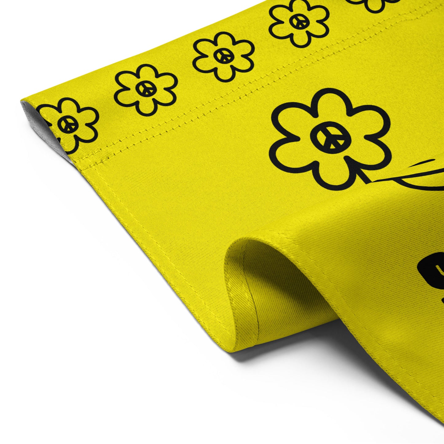 Close-up of yellow garden flag fabric showing stitched hem and repeating flower border pattern along top edge, detail view of bold black line-art design.