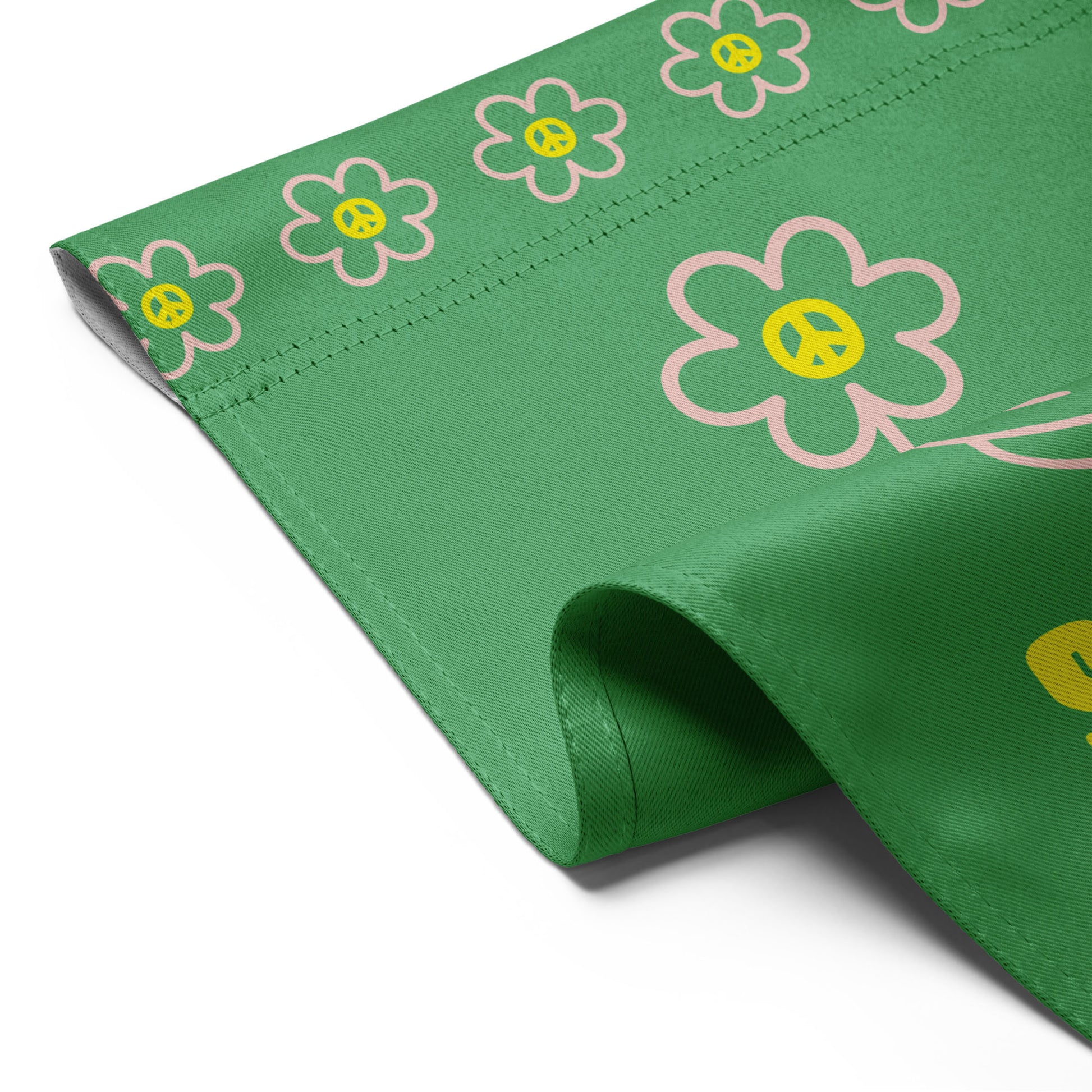 Close-up of green garden flag fabric showing stitched hem, repeating flower border along top edge, and partial “Stop the War Now!” text.