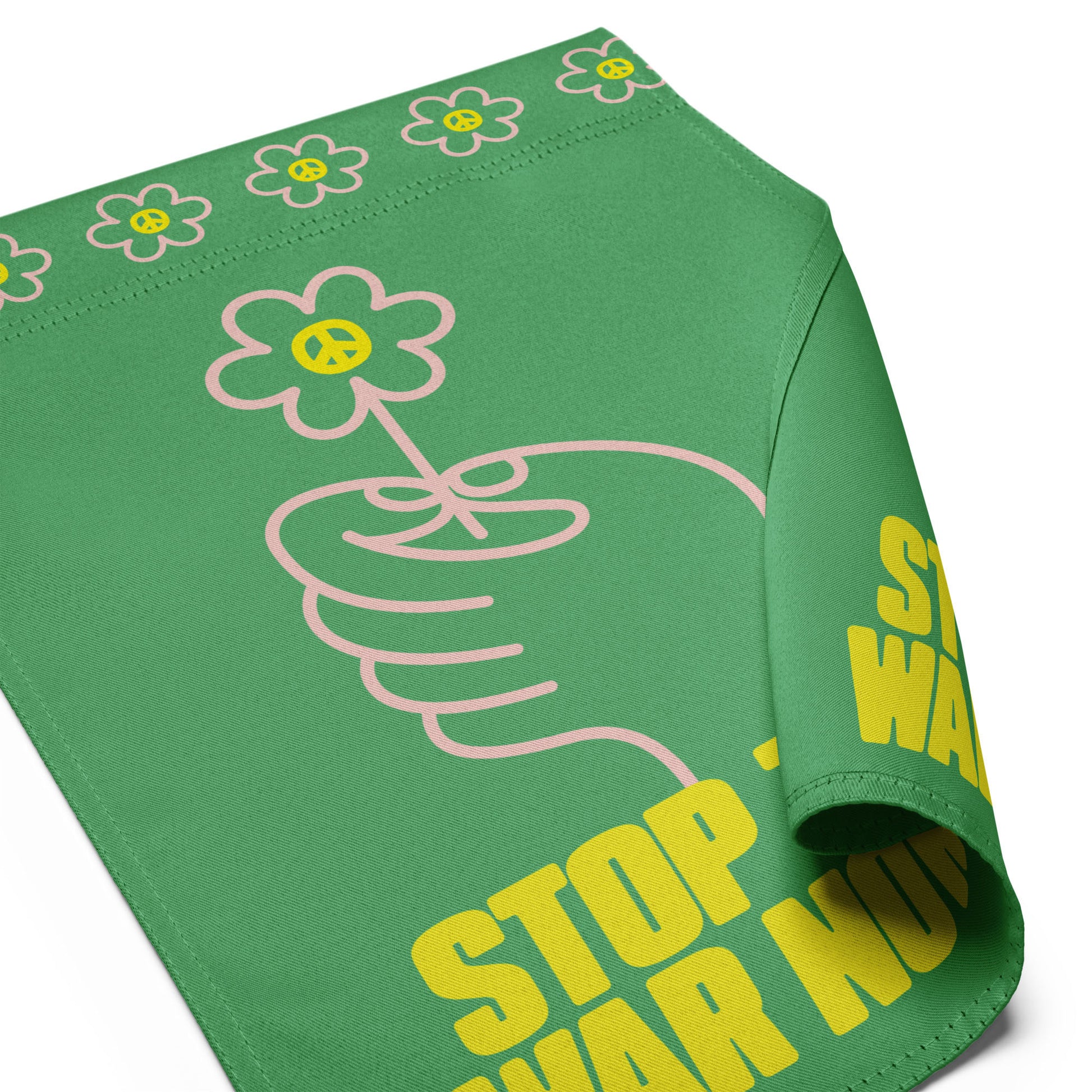 Angled close-up of green garden flag showing curved hem, floral border detail, and cropped yellow protest lettering near bottom edge.