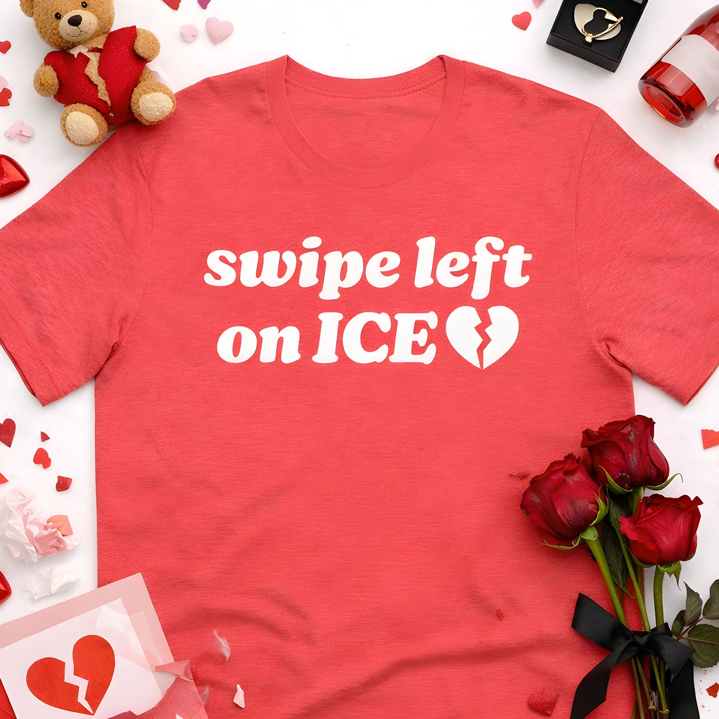 Unisex heather red t-shirt flat lay surrounded by roses and Valentine props, featuring bold white lettering and broken-heart icon with the phrase “swipe left on ICE,” activist apparel design.