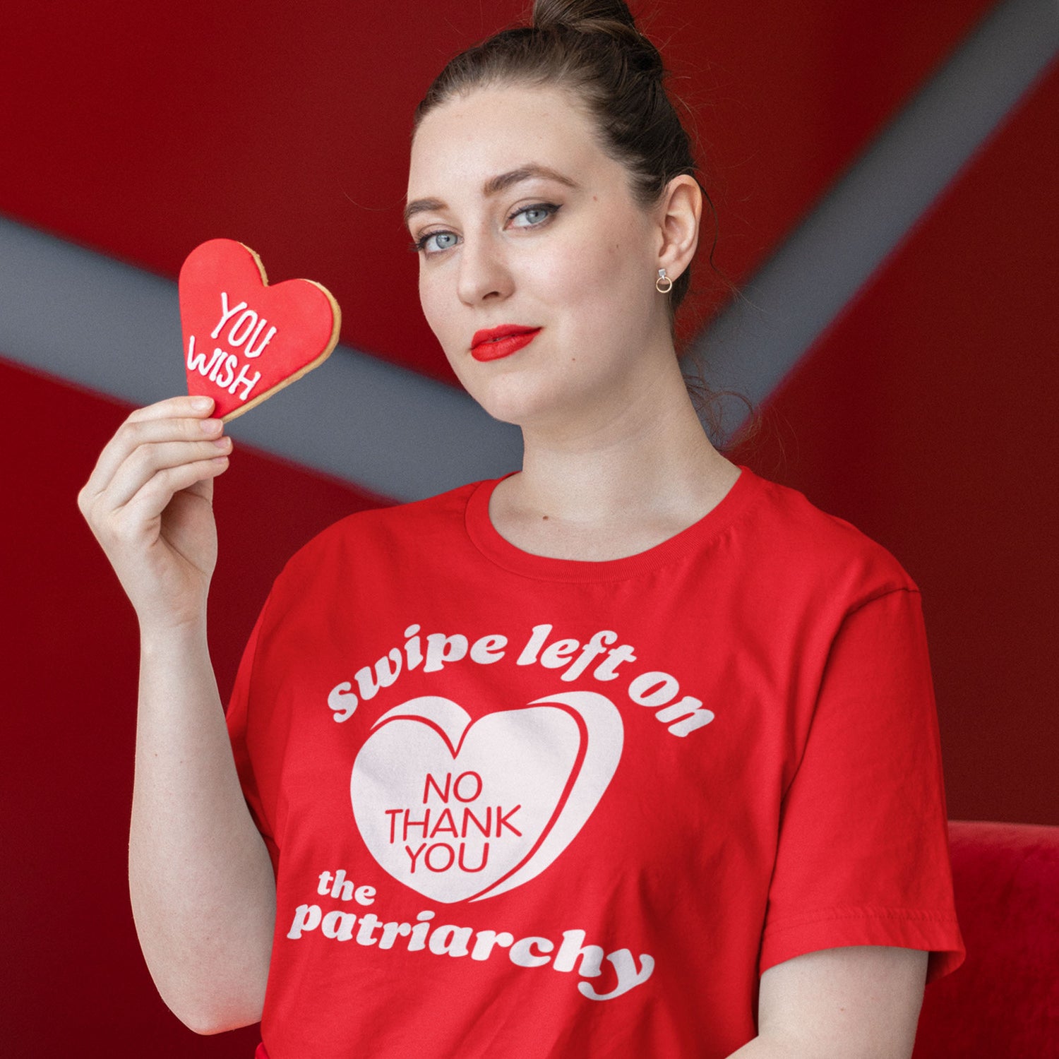 Woman wearing a red unisex t-shirt with heart graphic and bold lettering reading “swipe left on the patriarchy,” a justice-focused design from Blue Wave USA styled for activism.