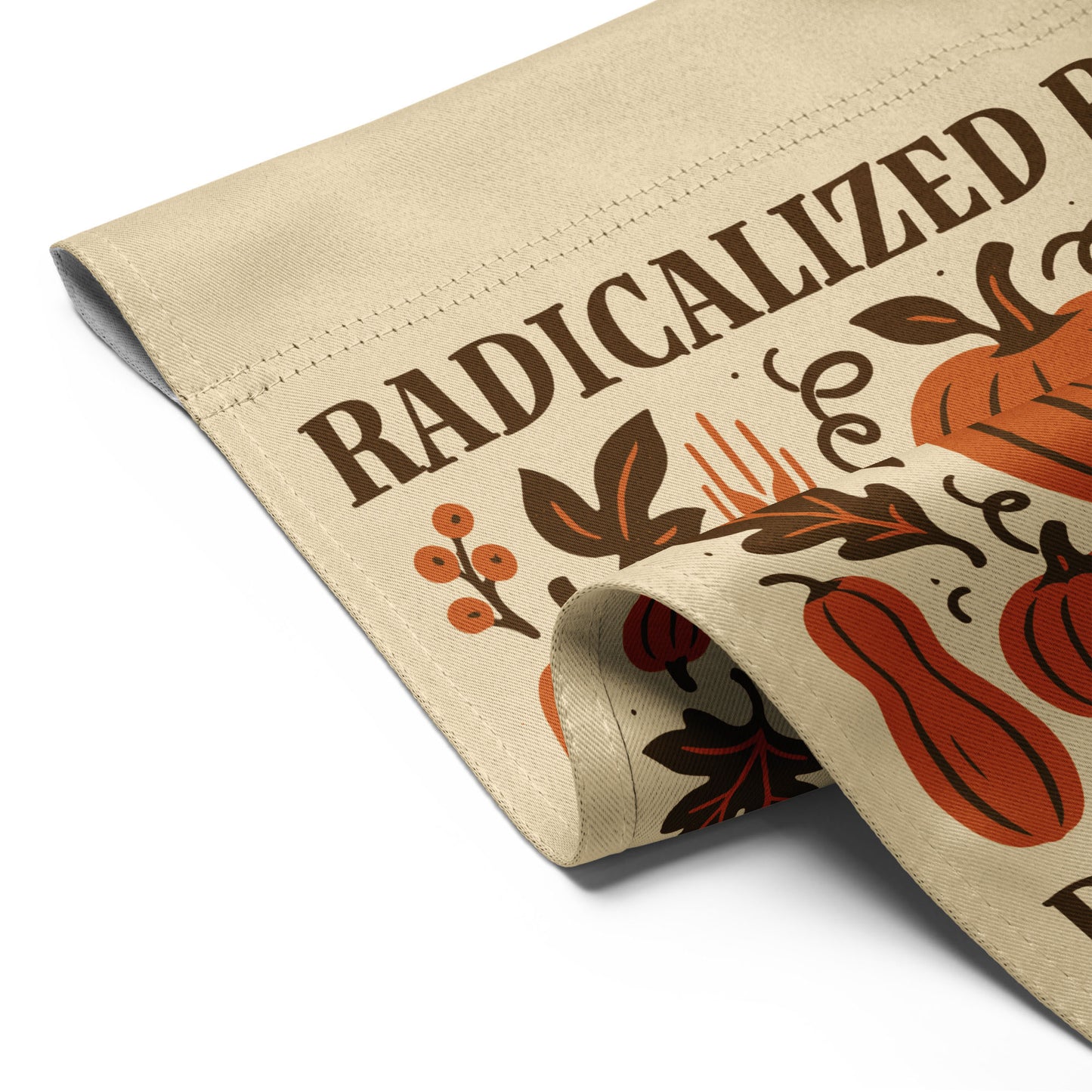 Folded garden flag showing pumpkin and leaf illustration with partial “Radicalized by Basic Decency” message, highlighting fabric texture and print detail.