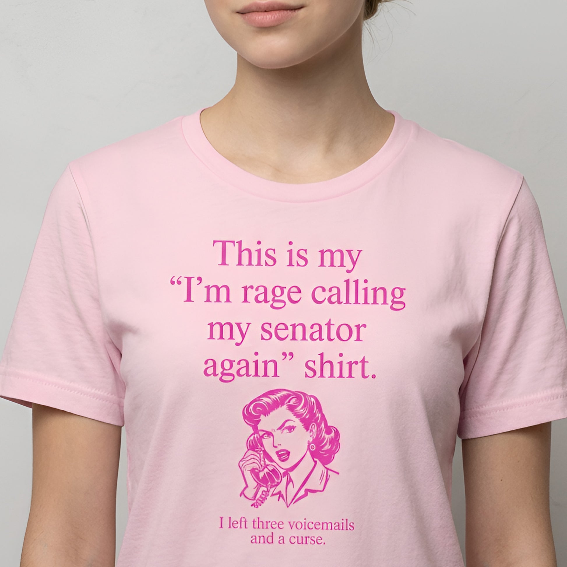 Model wearing light pink unisex t-shirt displaying pink text reading “This is my ‘I’m rage calling my senator again’ shirt.”
