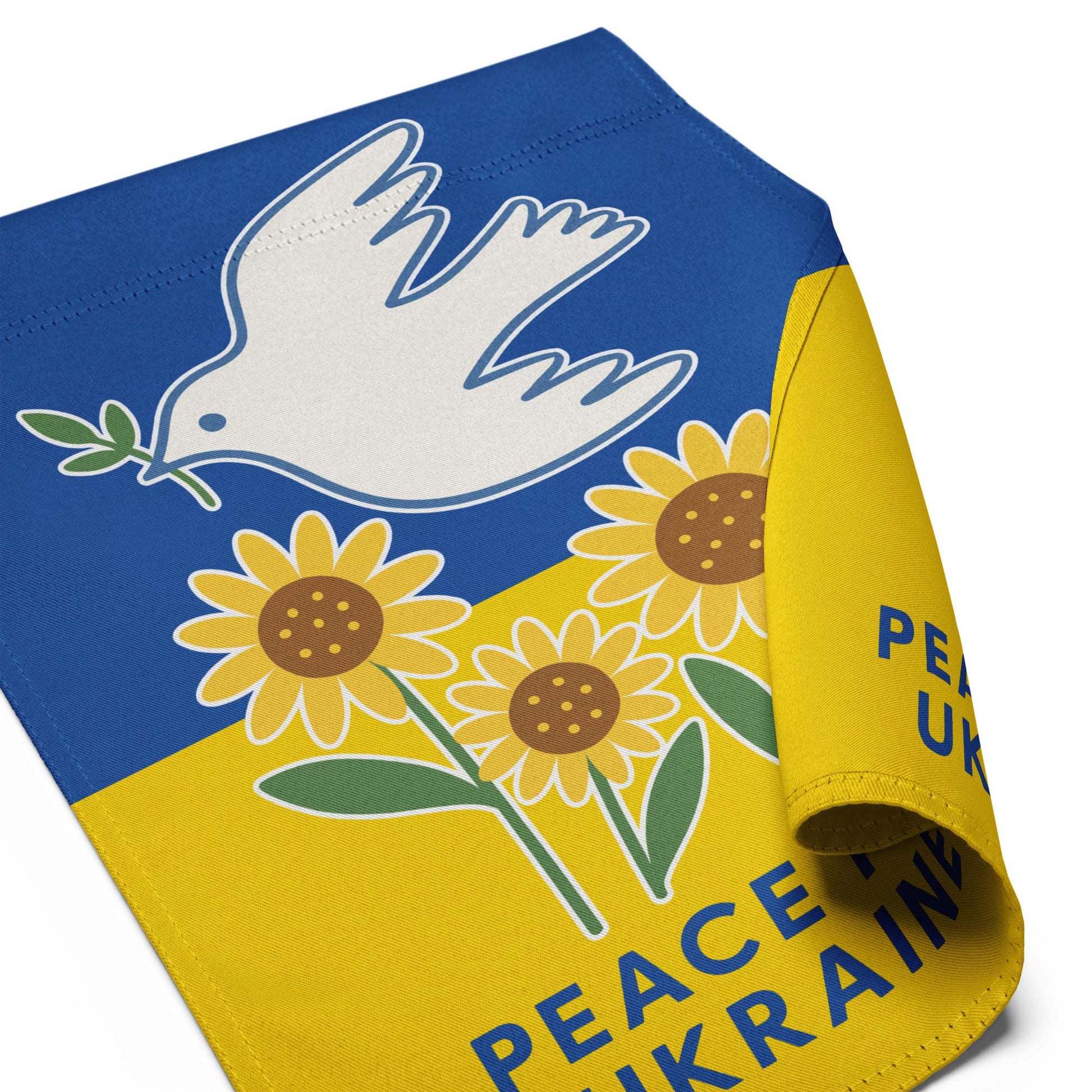 Close-up of the “Peace for Ukraine” activist garden flag with curled edge, showing dove and sunflower detail, Blue Wave USA progressive décor.