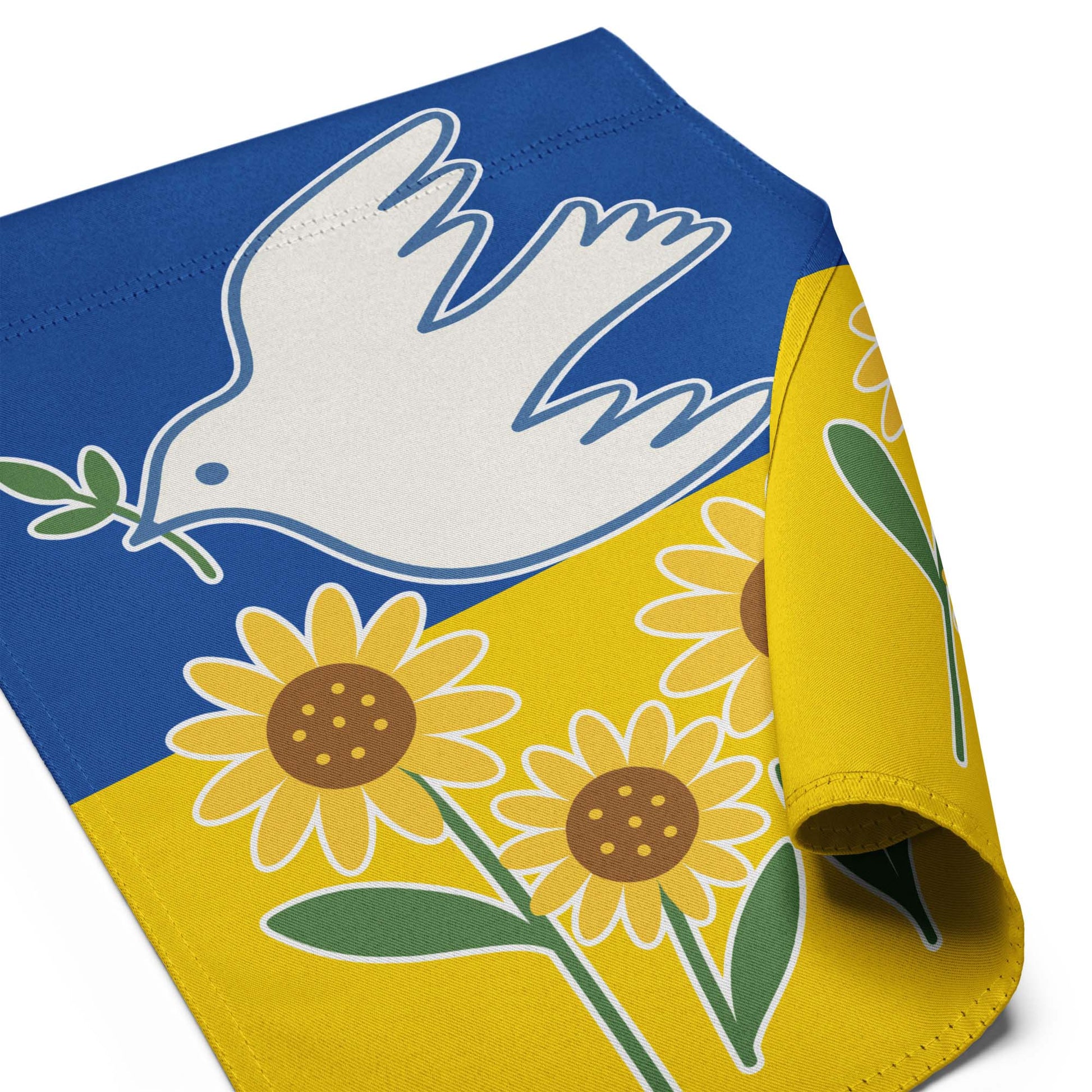 Angled close-up view of the Ukraine Solidarity garden flag with curled corner showing sunflower and blue sky background.