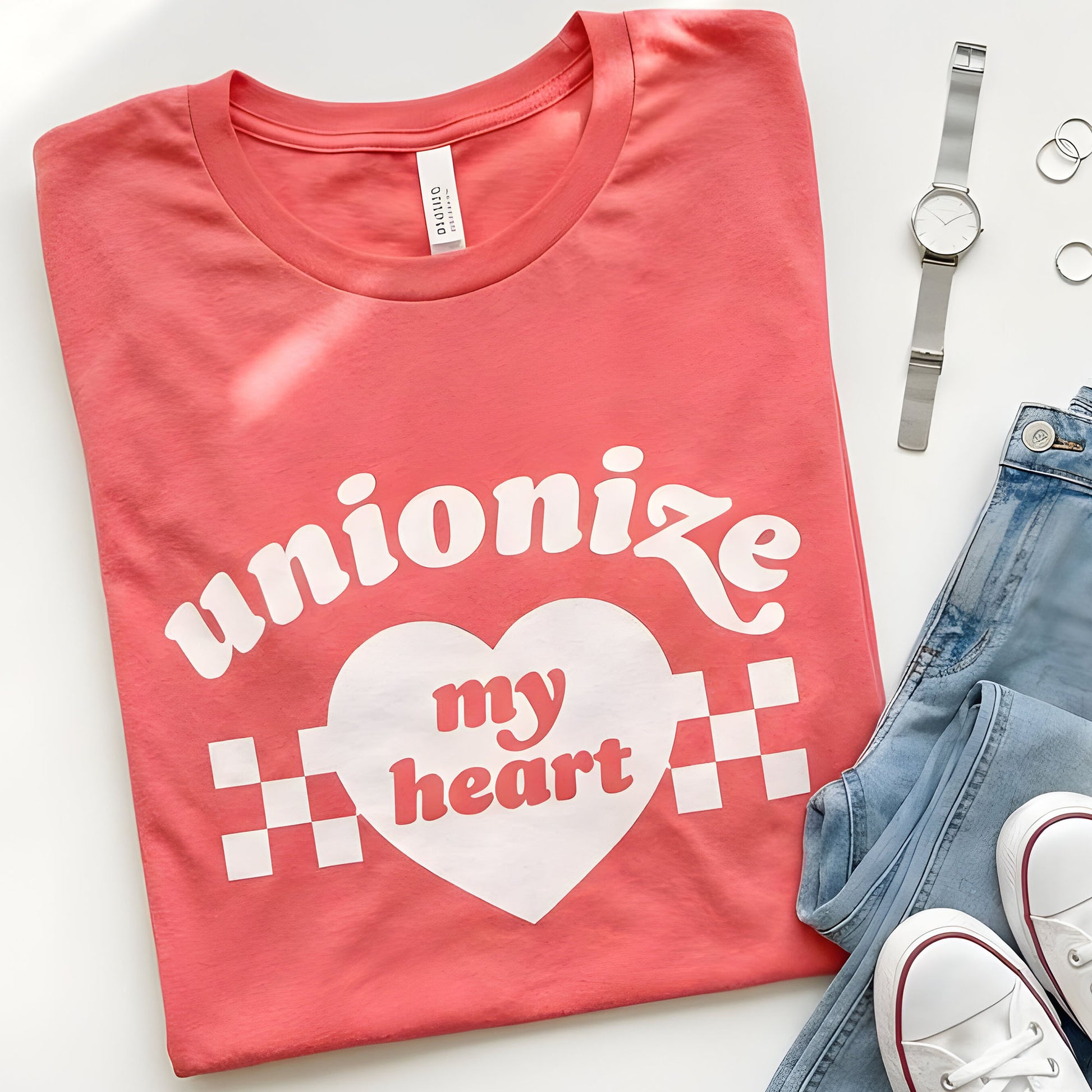 Unisex t-shirt featuring heart graphic with checkerboard accents and phrase “Unionize My Heart,” shown in heather red laid flat with denim and accessories by Blue Wave USA.