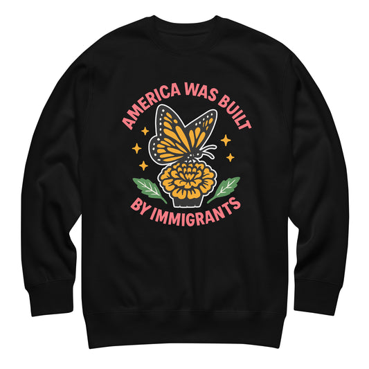 Black sweatshirt with “America Was Built by Immigrants” monarch butterfly and marigold design, activist apparel promoting immigrant pride.