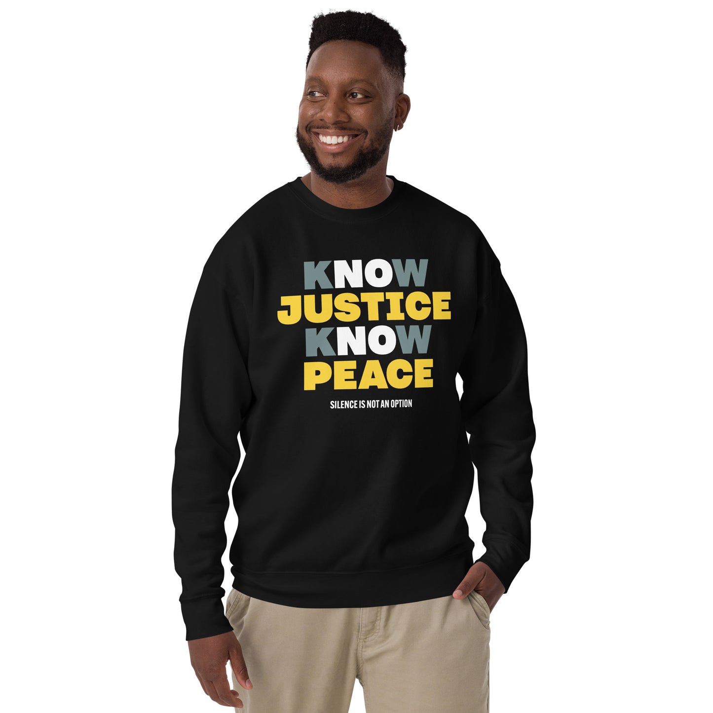 Person standing and smiling in the black Know Justice Know Peace sweatshirt, the bold yellow and white text bright against the dark fabric — a confident, unifying statement of equality and action.