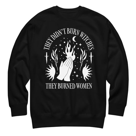 Unisex premium sweatshirt featuring occult-inspired illustration of raised hands, flames, stars, and crescent moons, high-contrast white graphic, printed message “THEY DIDN’T BURN WITCHES THEY BURNED WOMEN,” black fabric.