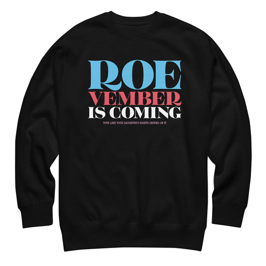 Black unisex premium sweatshirt featuring bold red, white, and blue typography reading “Roevember Is Coming,” reproductive rights activist apparel from Blue Wave USA.