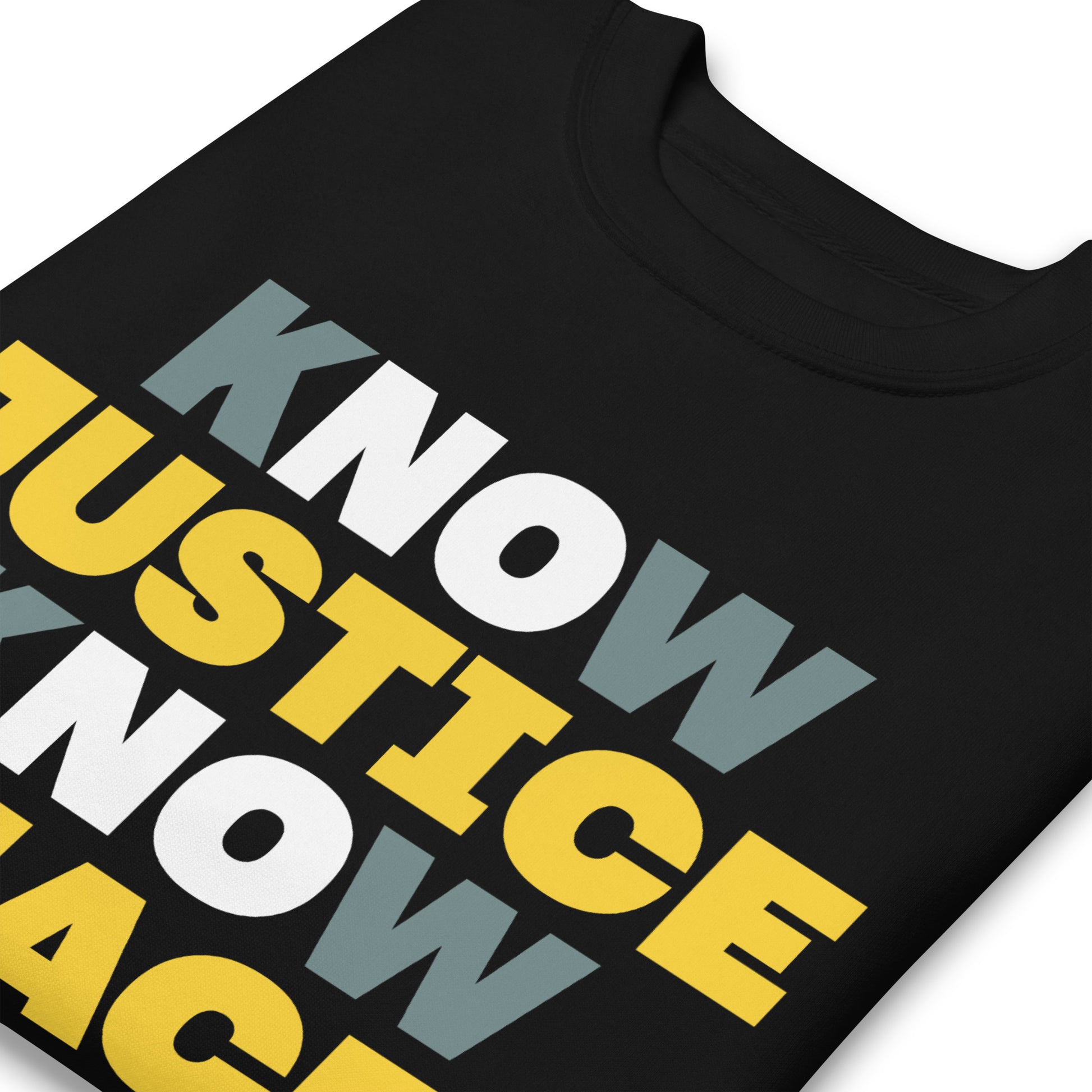 Close-up of the Know Justice Know Peace print on a black sweatshirt, showing the smooth texture of the material and the clean contrast between gold and gray lettering.