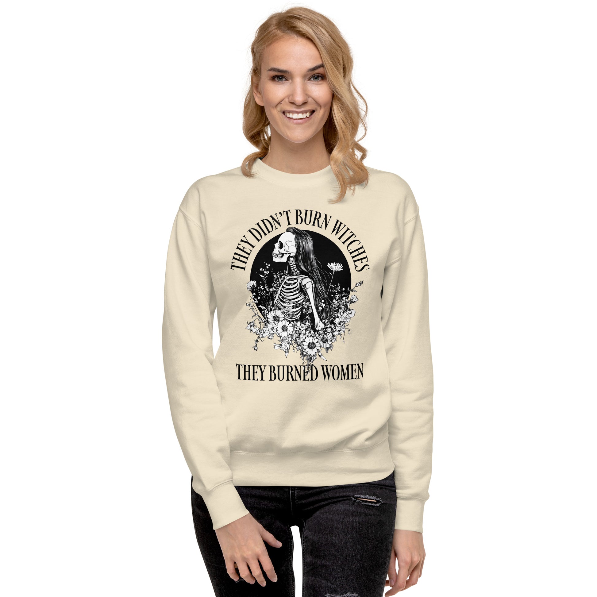 Model wearing cream unisex premium sweatshirt with intricate witch-inspired skeleton illustration, vintage gothic style, centered layout, printed message “THEY DIDN’T BURN WITCHES THEY BURNED WOMEN.”