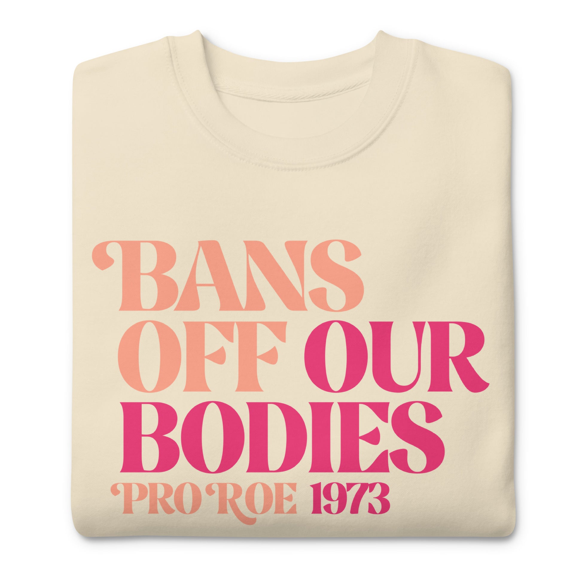 Folded cream unisex premium sweatshirt featuring bold vintage-style serif typography in pink gradient tones, centered layout, printed message “BANS OFF OUR BODIES PRO ROE 1973.”