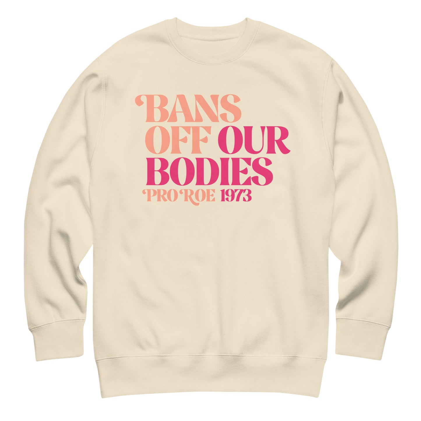 Cream unisex premium sweatshirt laid flat showing bold retro serif lettering in pink gradient, centered chest placement, printed message “BANS OFF OUR BODIES PRO ROE 1973.”