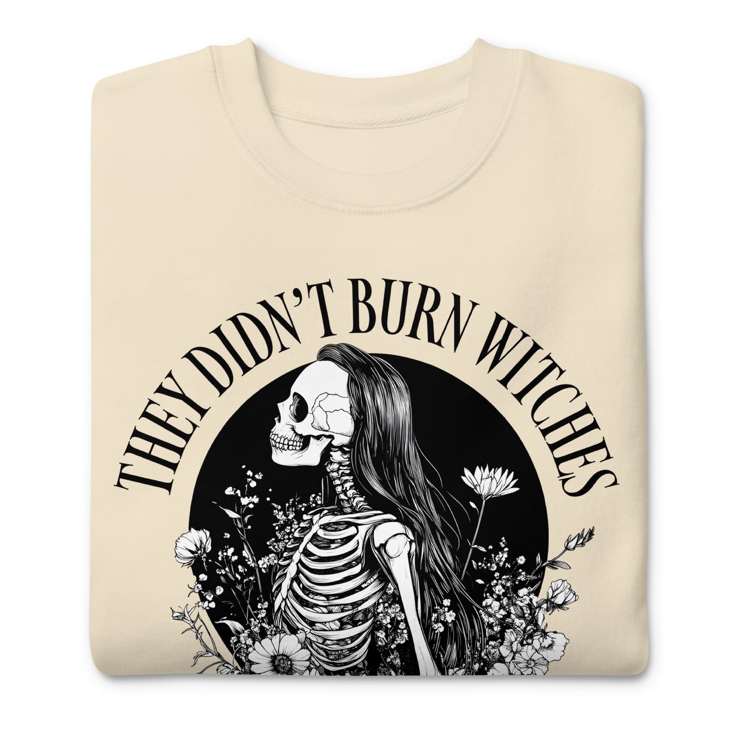 Folded cream unisex premium sweatshirt featuring detailed skeleton and witch illustration in black ink, circular composition, printed message “THEY DIDN’T BURN WITCHES THEY BURNED WOMEN.”