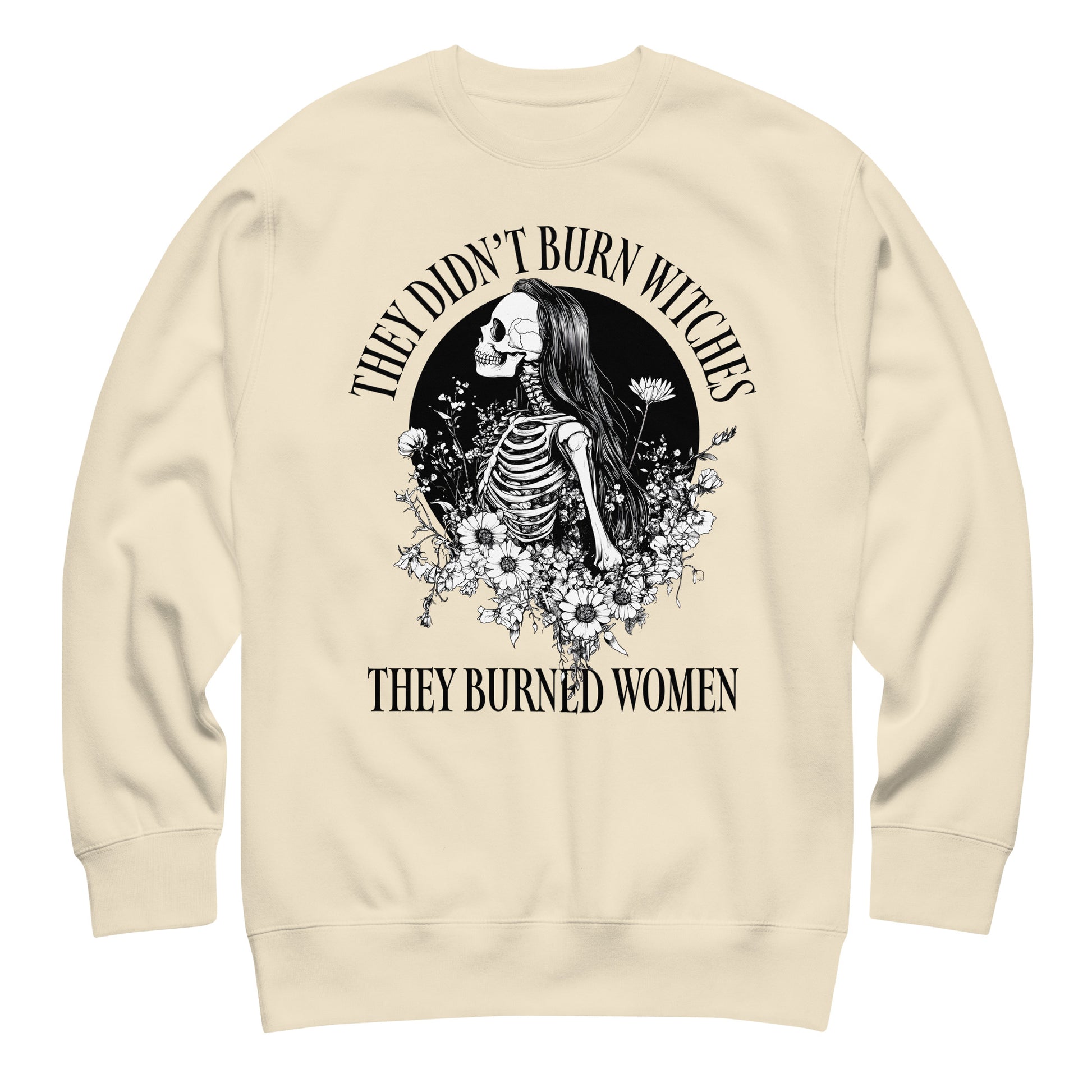 Cream unisex premium sweatshirt laid flat showing ornate skeleton illustration with floral details, high-contrast black print, printed message “THEY DIDN’T BURN WITCHES THEY BURNED WOMEN,” progressive apparel from Blue Wave USA.