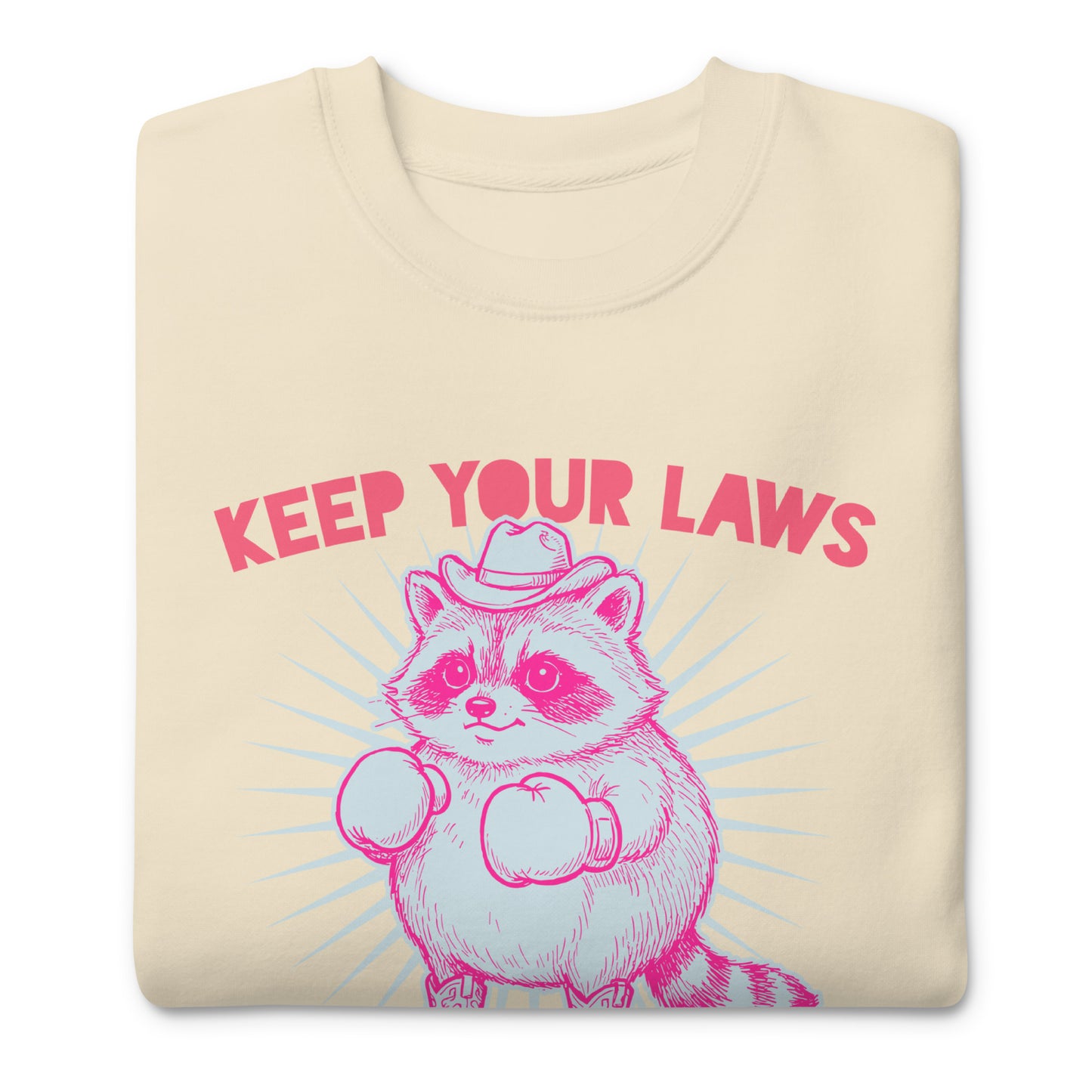 Folded cream sweatshirt displaying cowboy raccoon artwork with “Off My Body” phrase in bold reproductive rights protest style.