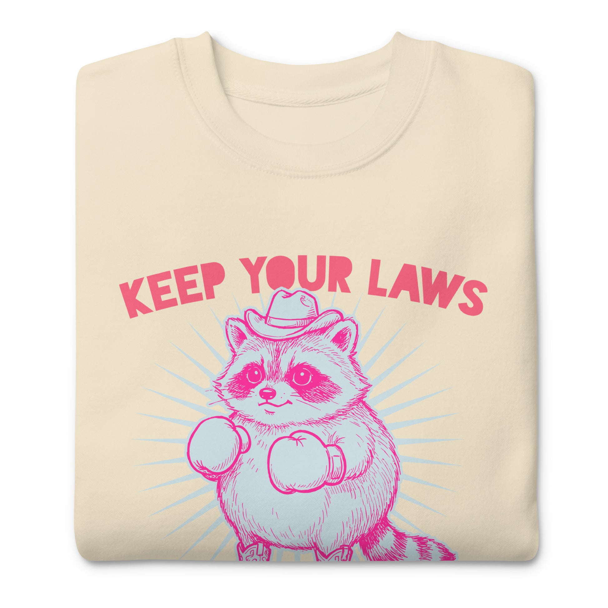 Folded cream sweatshirt displaying cowboy raccoon artwork with “Off My Body” phrase in bold reproductive rights protest style.